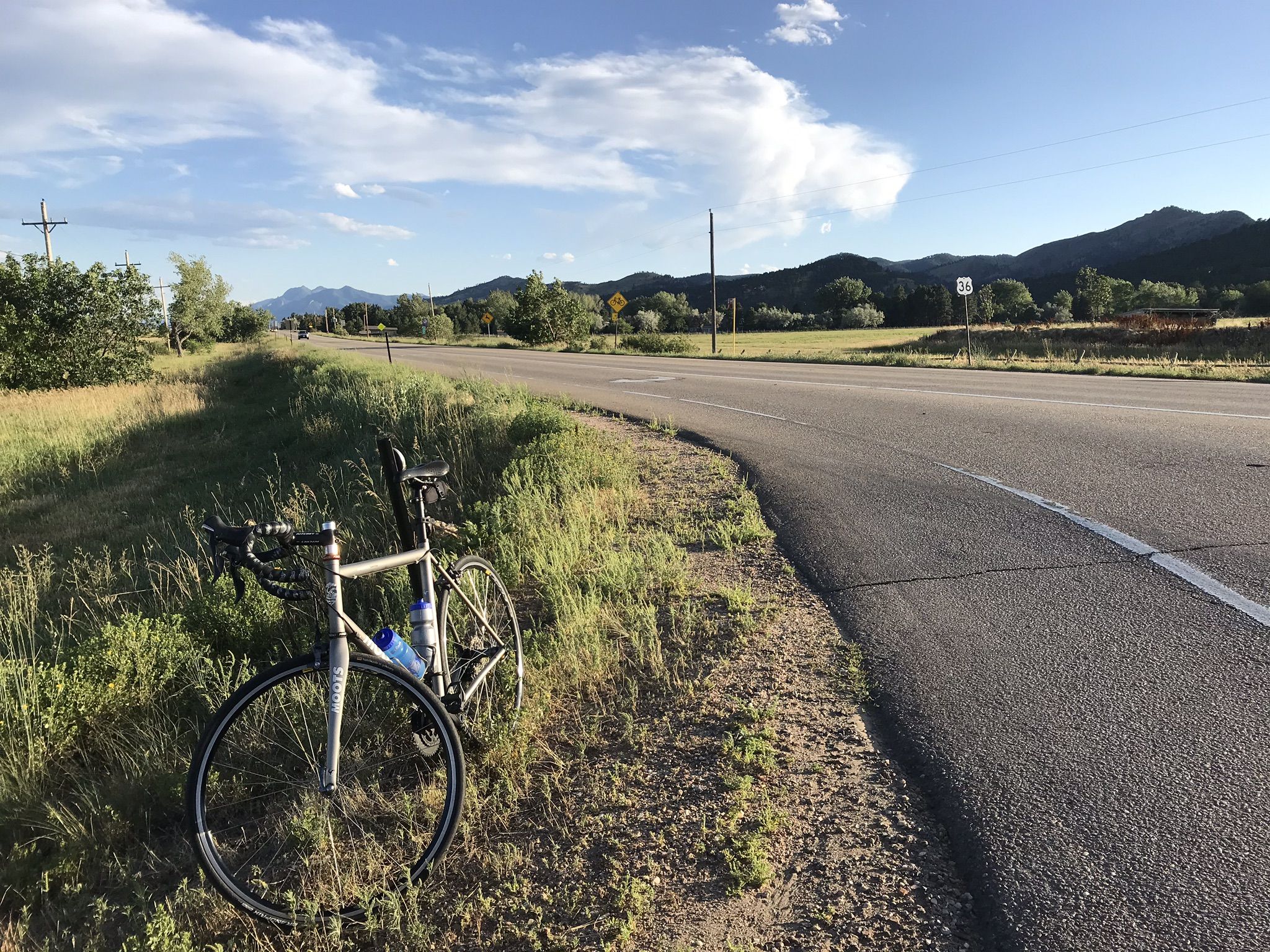 Bicycle parked on a grassy road shoulder with distant mountains under a cloudy sky. - The Mountain Fountain – Main Street loop from Bus 323, 324