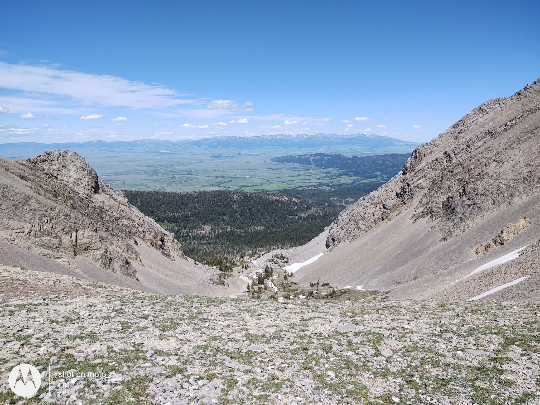 Steep rocky mountain valley opens to distant green plains under blue sky. - Sacagawea Peak via North Cottonwood Trail