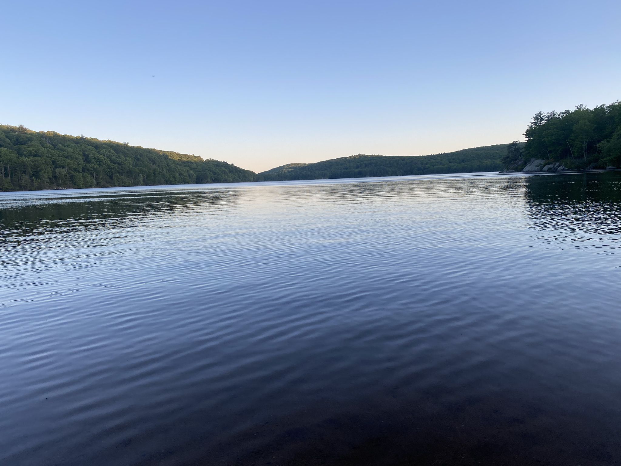 Expansive calm lake surrounded by green forested hills under a clear sky. - Sterling Lake Loop Trail
