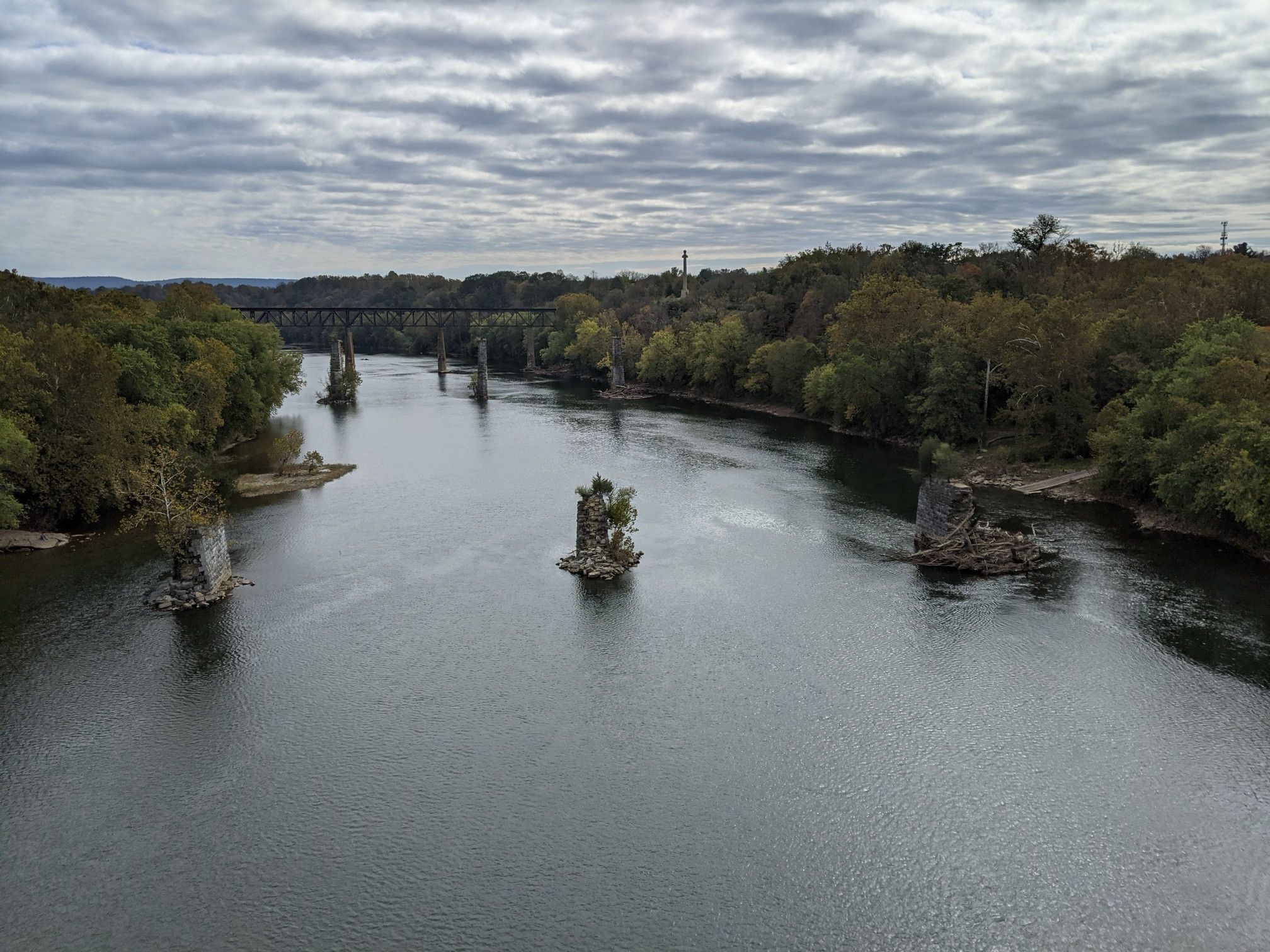 Overcast view of a wide river with old bridge piers and a distant bridge. - Shepherdstown and Williamsport C&O Canal Loop