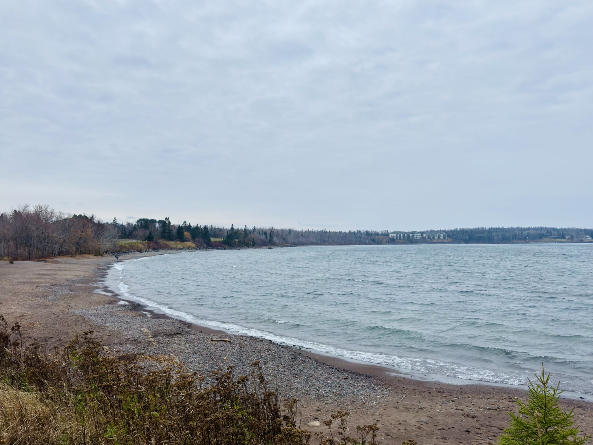 A rocky beach curves along calm water under a cloudy sky. - Knife River loop from Two Harbors