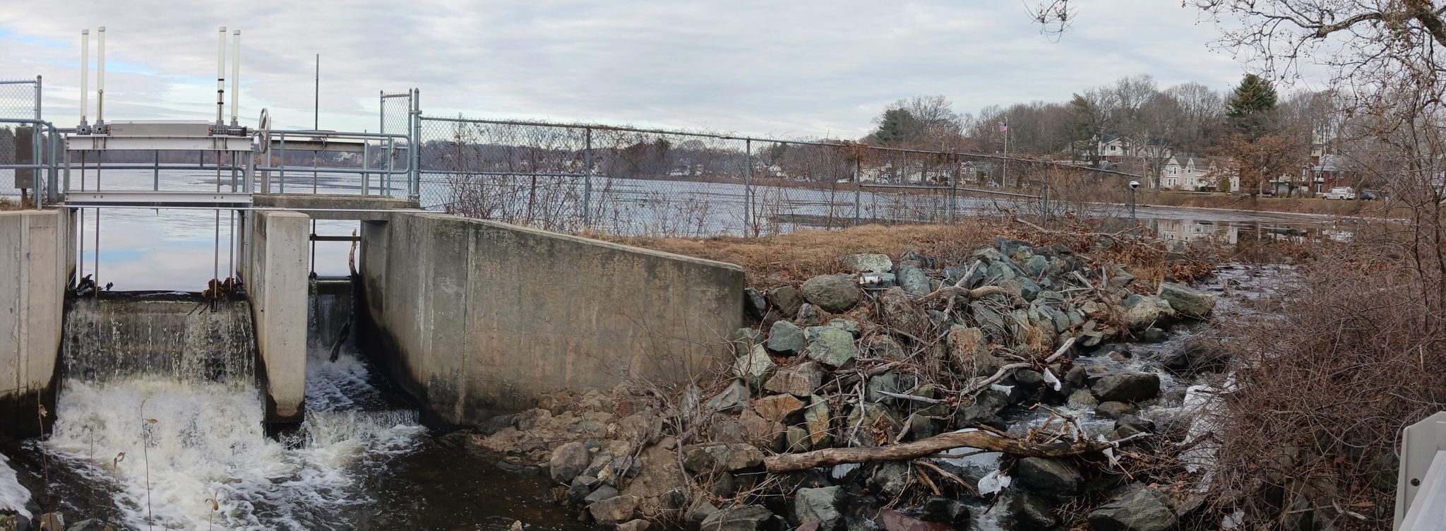Concrete dam with water flowing, rocky bank, under an overcast sky. - Running loop from Woburn