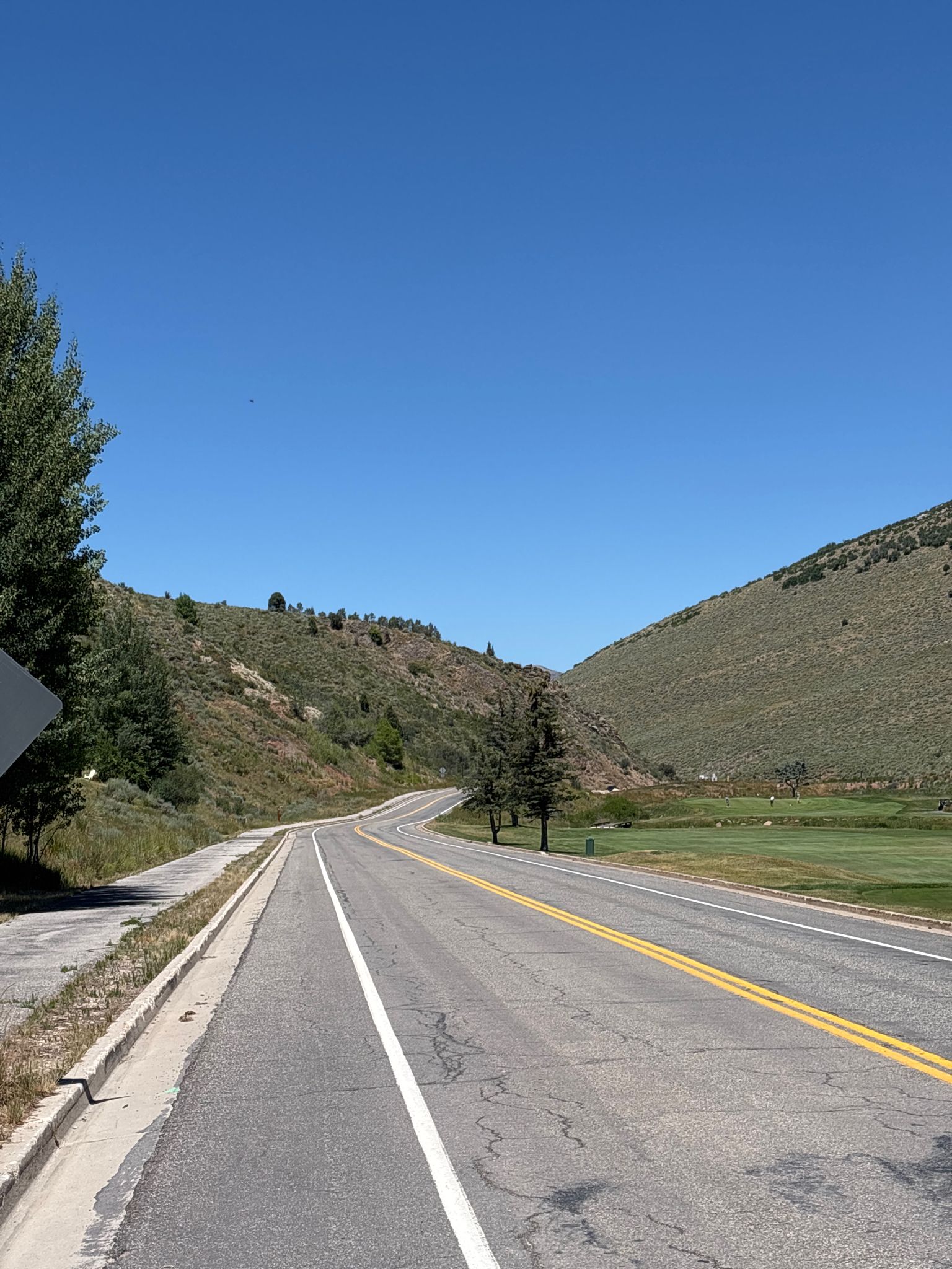 Winding road through a valley with green hills and trees under blue sky. - A – Big Mountain Pass loop from Summit Park