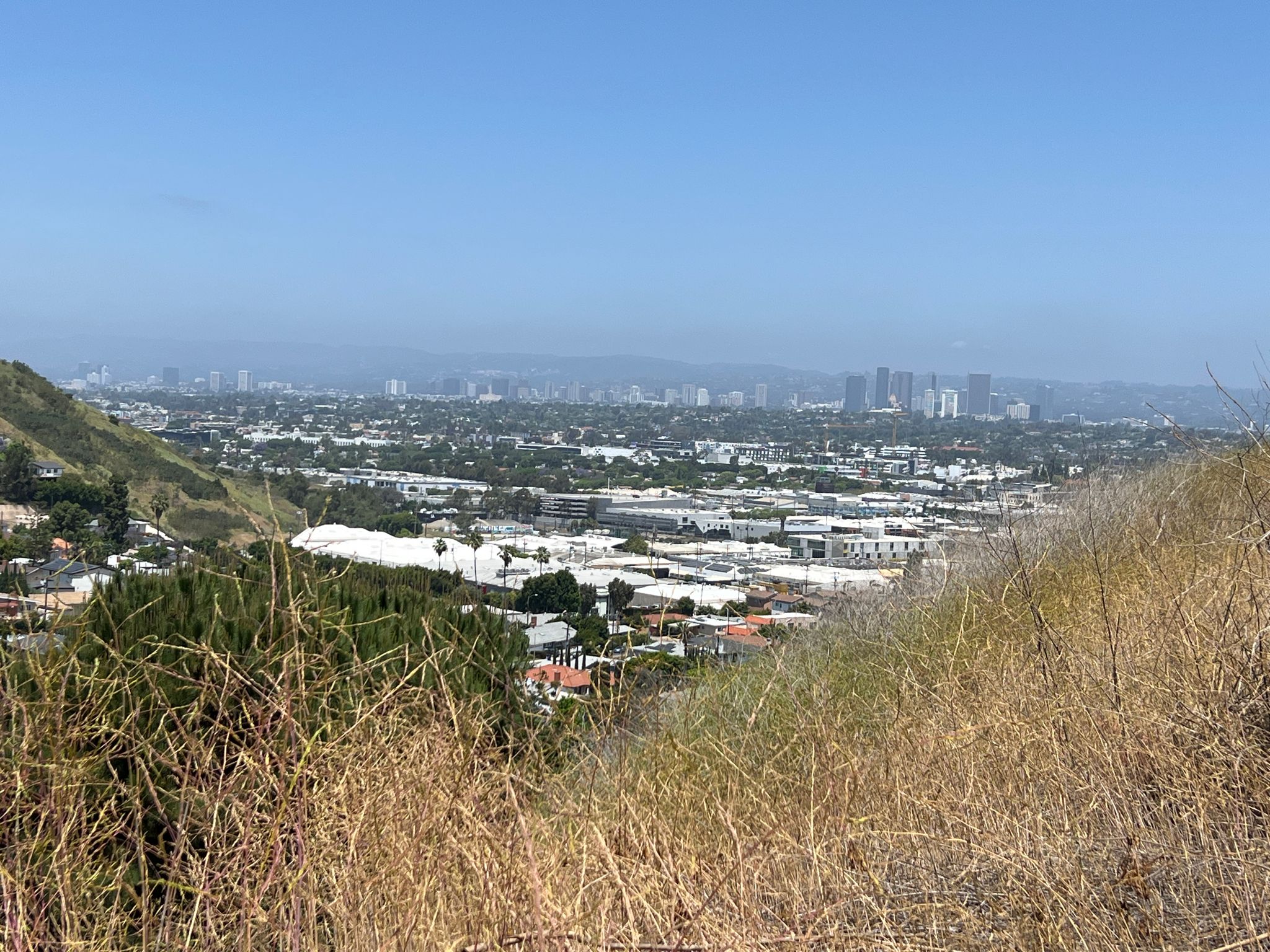 Hazy panoramic view of a sprawling city from a dry, grassy hillside. - Vistas, waterfall, lake & memorial run – Kenneth Hahn State Recreational Area