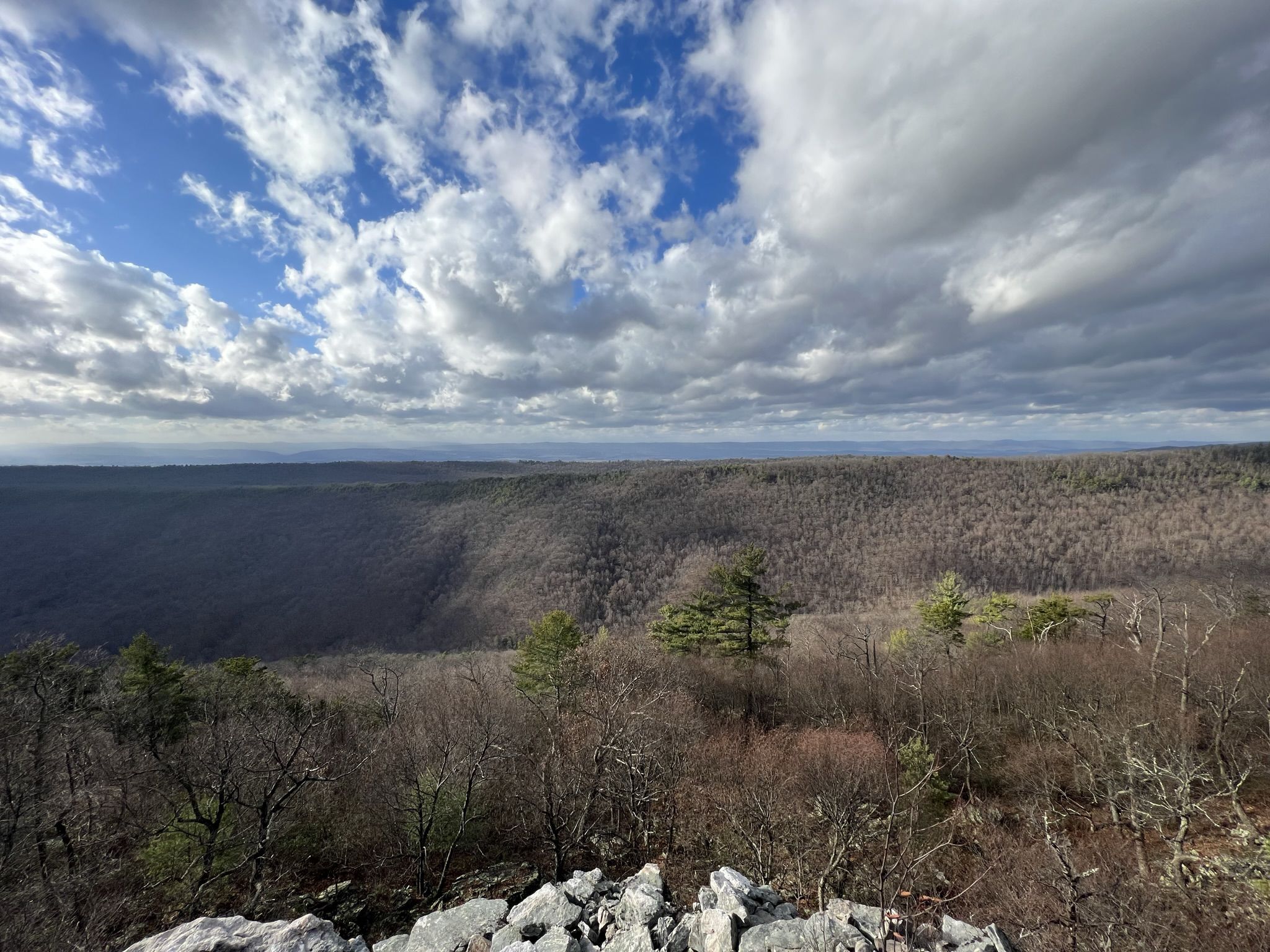 Vast forested valley under a dramatic cloudy sky, with rocky foreground. - Strickler Knob Trail