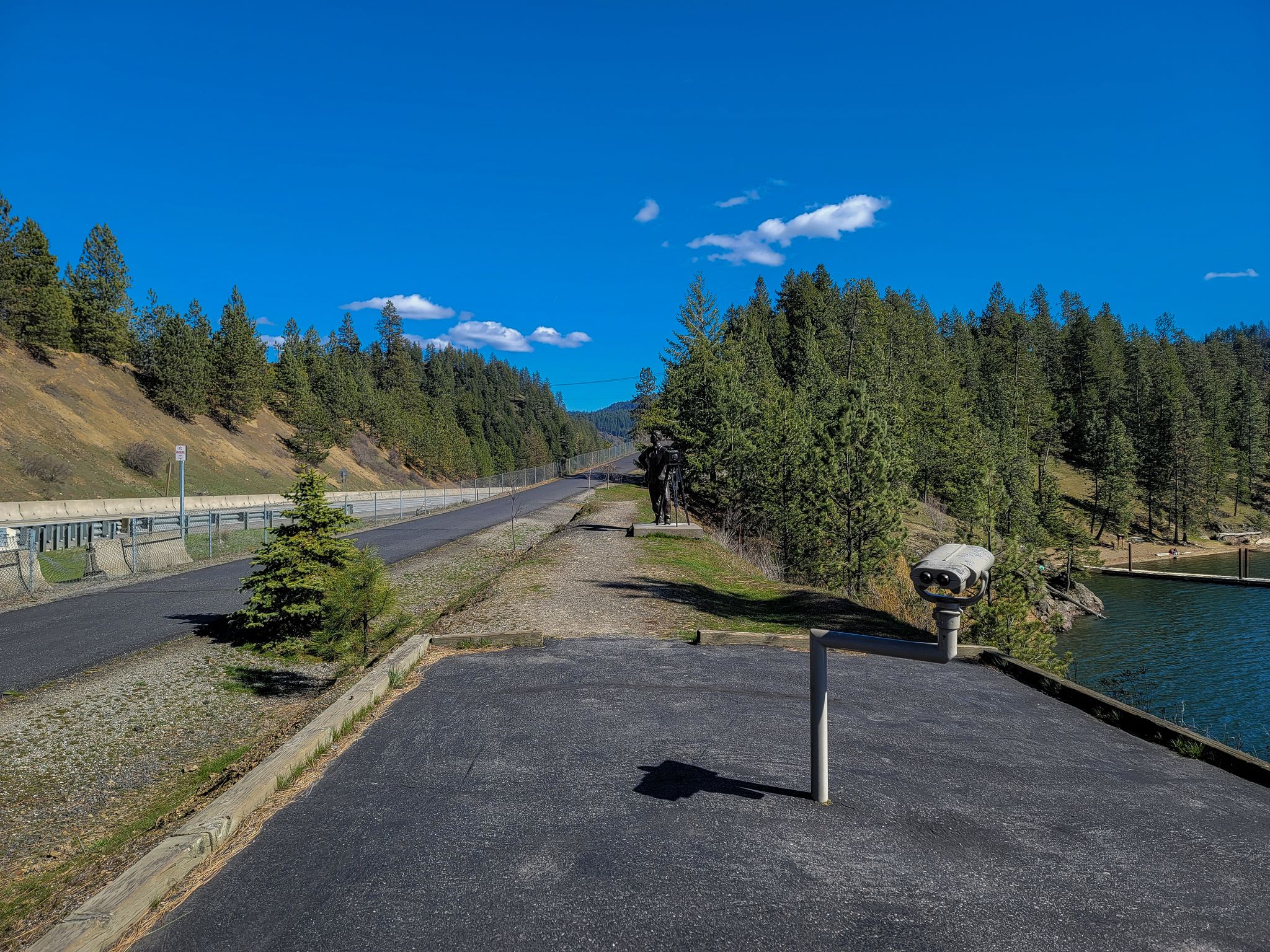 Paved road and viewing area overlooking a lake surrounded by pine trees. - North Idaho Centennial Trail and Fernan Lake Loop