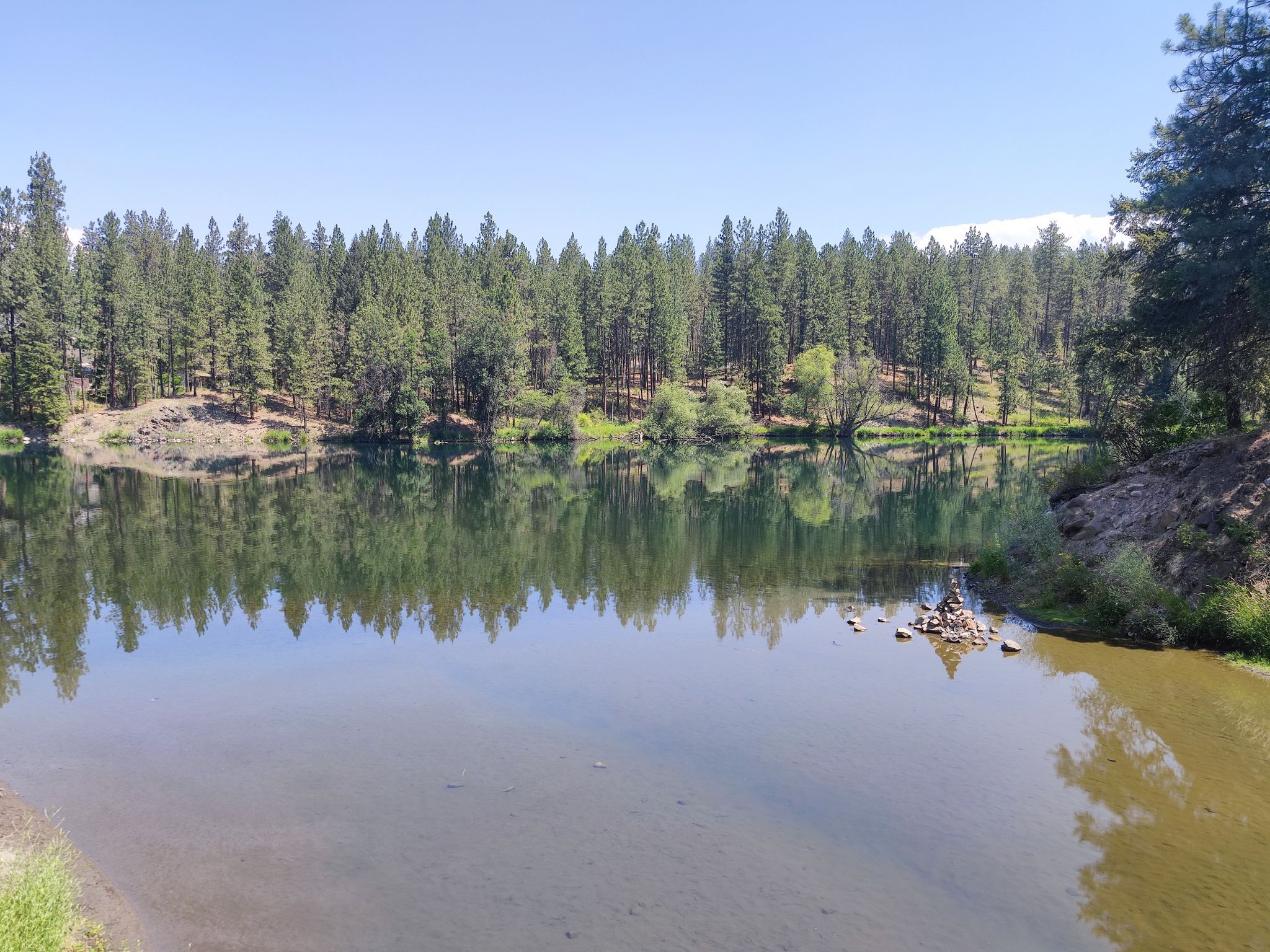 A tranquil lake reflecting a dense green forest under a clear blue sky. - Deep Creek Loop