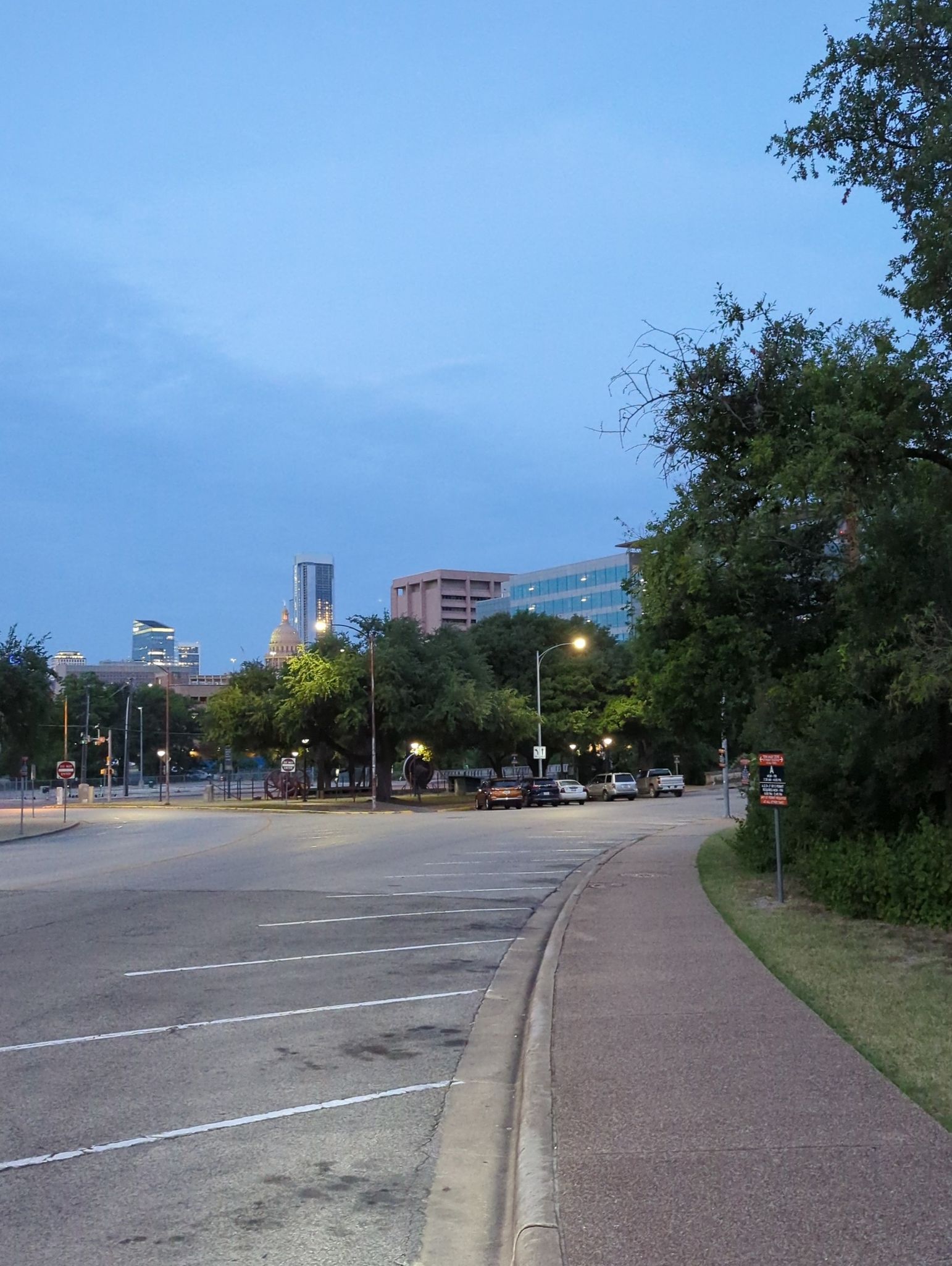 City skyline at dusk with a road, trees, and buildings under a blue sky. - Austin State Capitol Walking Tour