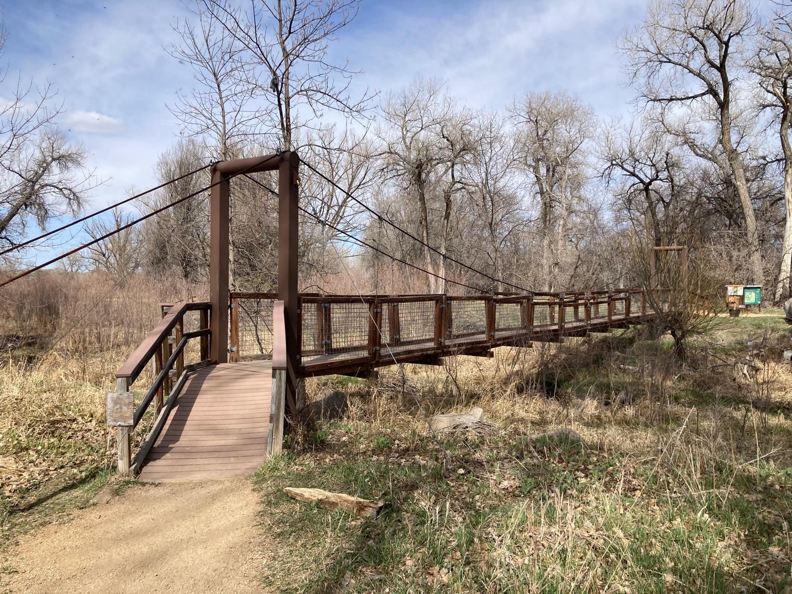 A wooden suspension bridge over dry grass with bare trees. - Arapaho Bend Natural Area – Rigden Reservoir loop from Timnath