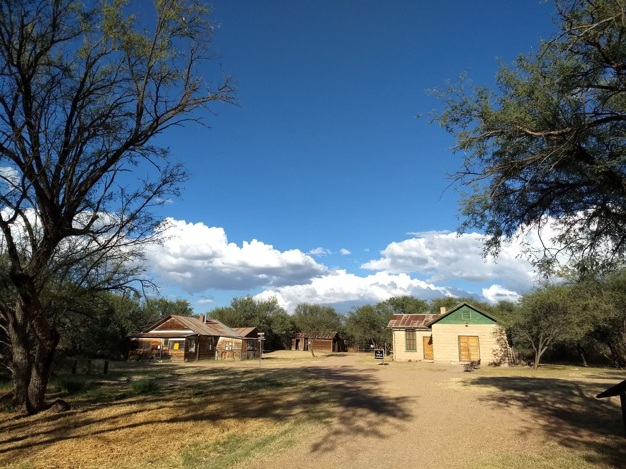 Old buildings and a dirt path surrounded by trees under a bright blue sky. - Fairbank Loop via San Pedro Trail