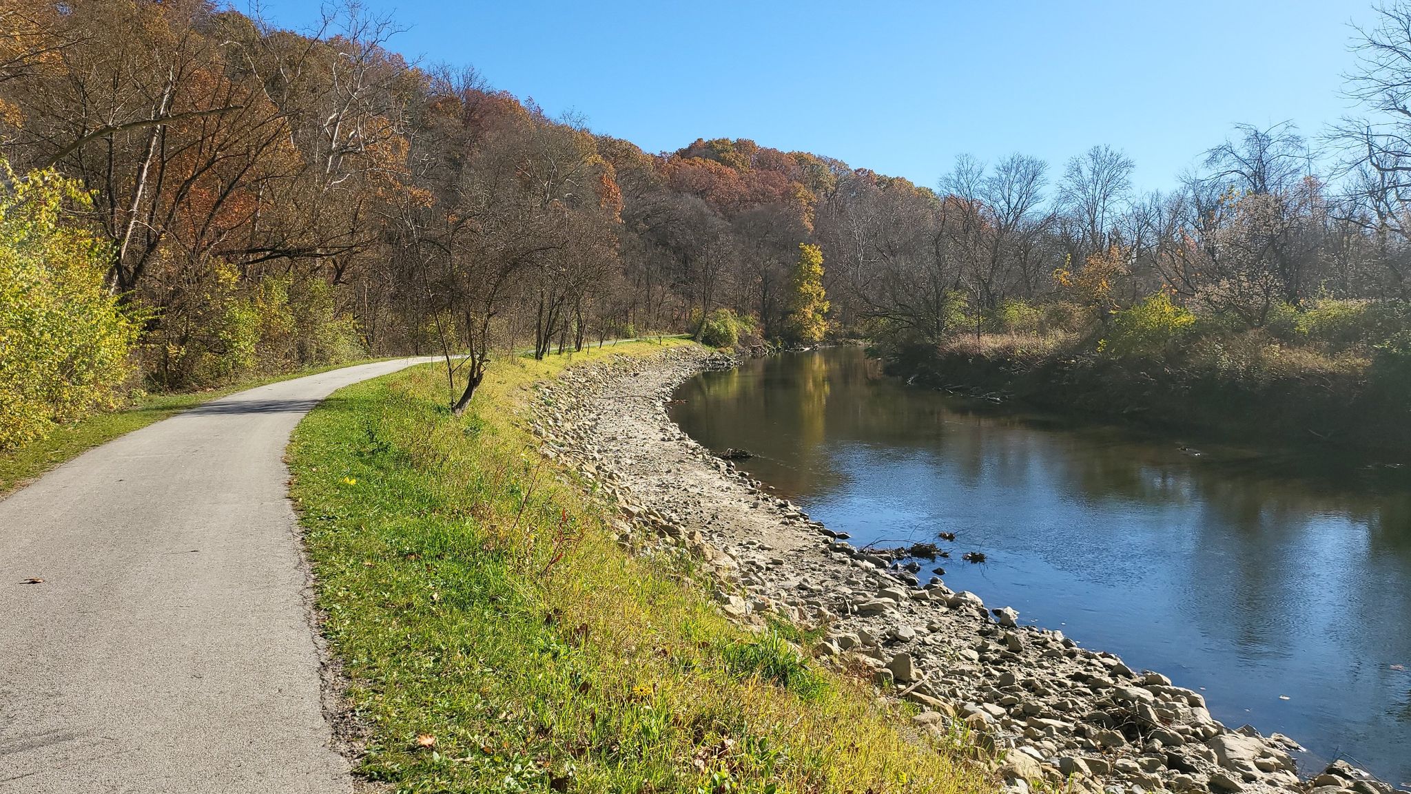 Paved path curves alongside a river, with autumn trees under a clear sky. - Lock 29 – Boston Trailhead loop from Peninsula