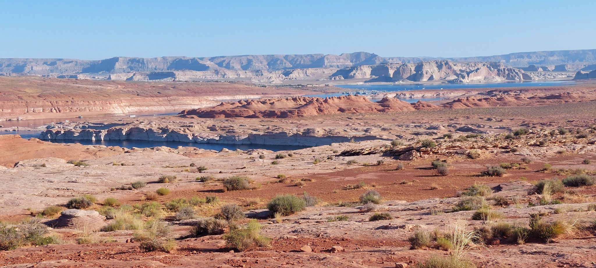 Expansive desert landscape with sparse vegetation, distant blue water, rock formations. - Rimview Trail