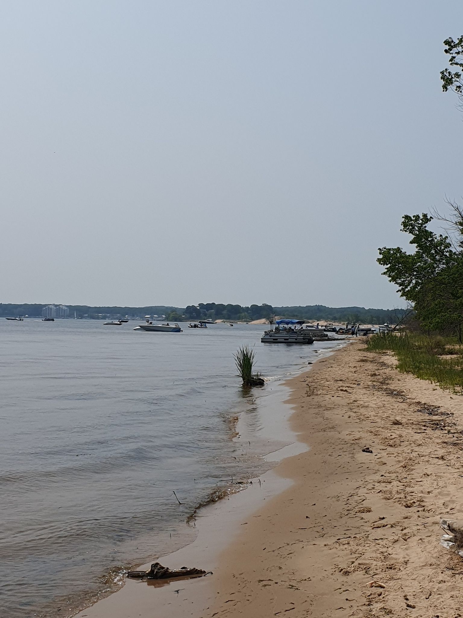 Sandy beach and calm water with distant boats under an overcast sky. - Muskegon Lake loop from Muskegon State Park