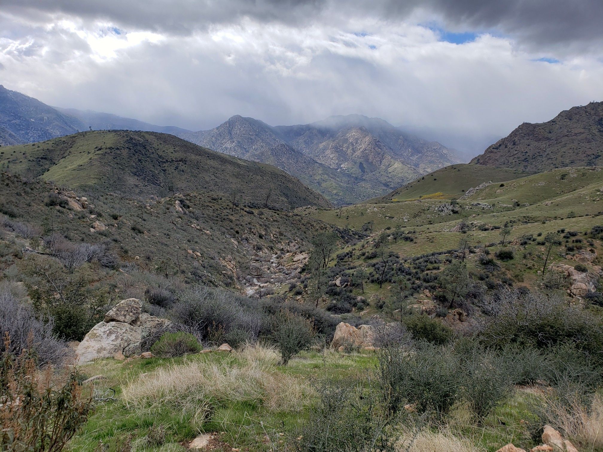 Green rolling hills and mountains under a dramatic, cloudy sky. - Powers Peak