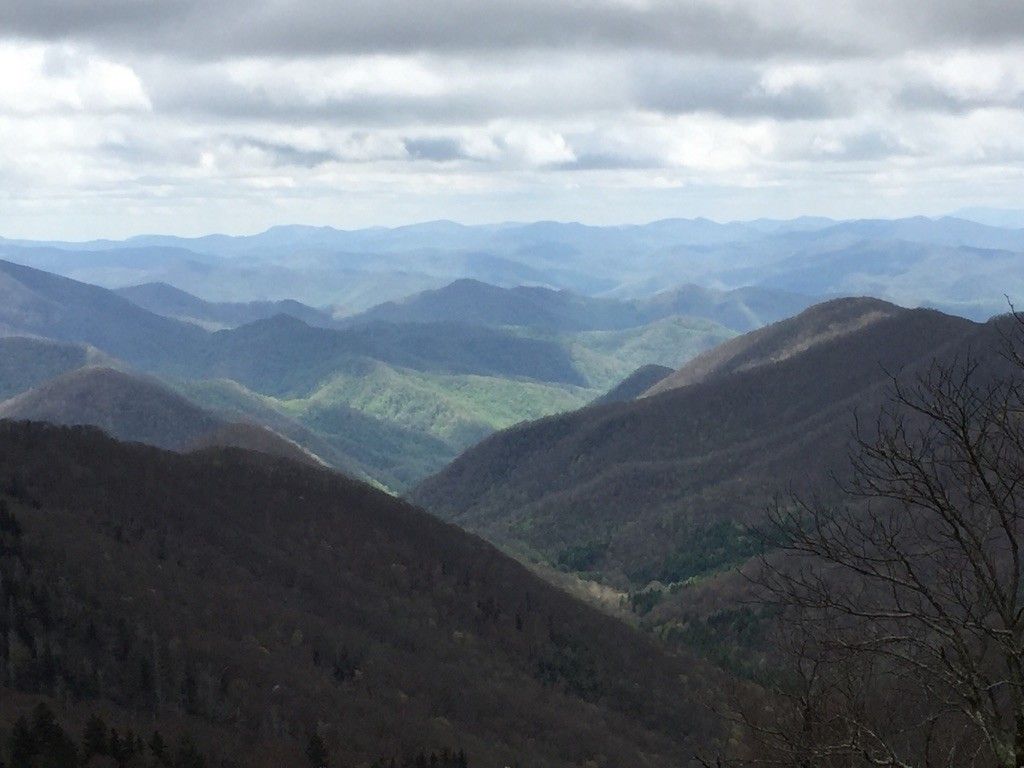 Hazy layers of forested mountains and valleys under a cloudy, bright sky. - Mountains to Sea Bicycle Route