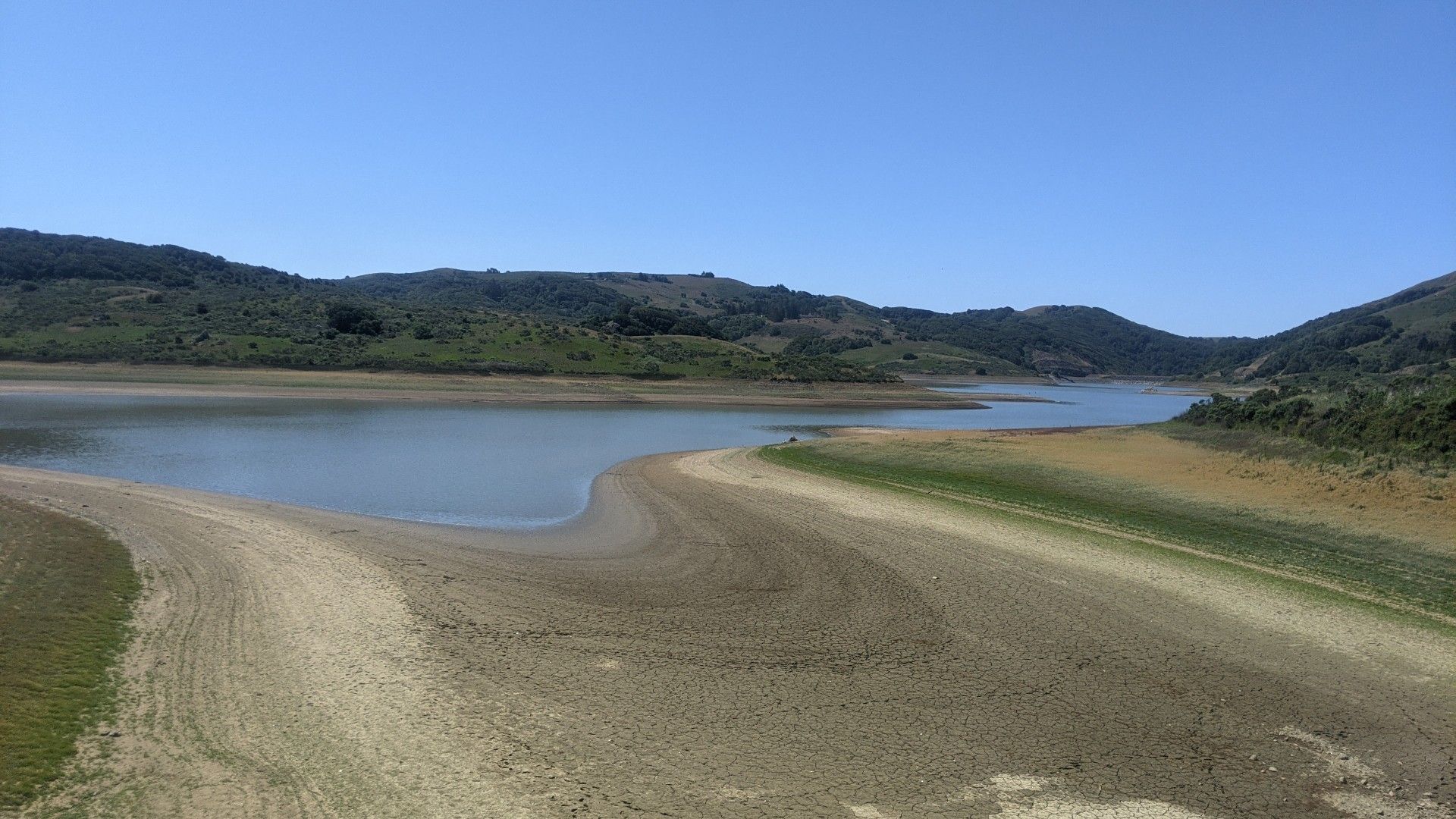 A wide lake with exposed sandy banks and green hills under a clear blue sky. - Point Reyes–Petaluma Bridge – Point Reyes Station loop from Petaluma Downtown