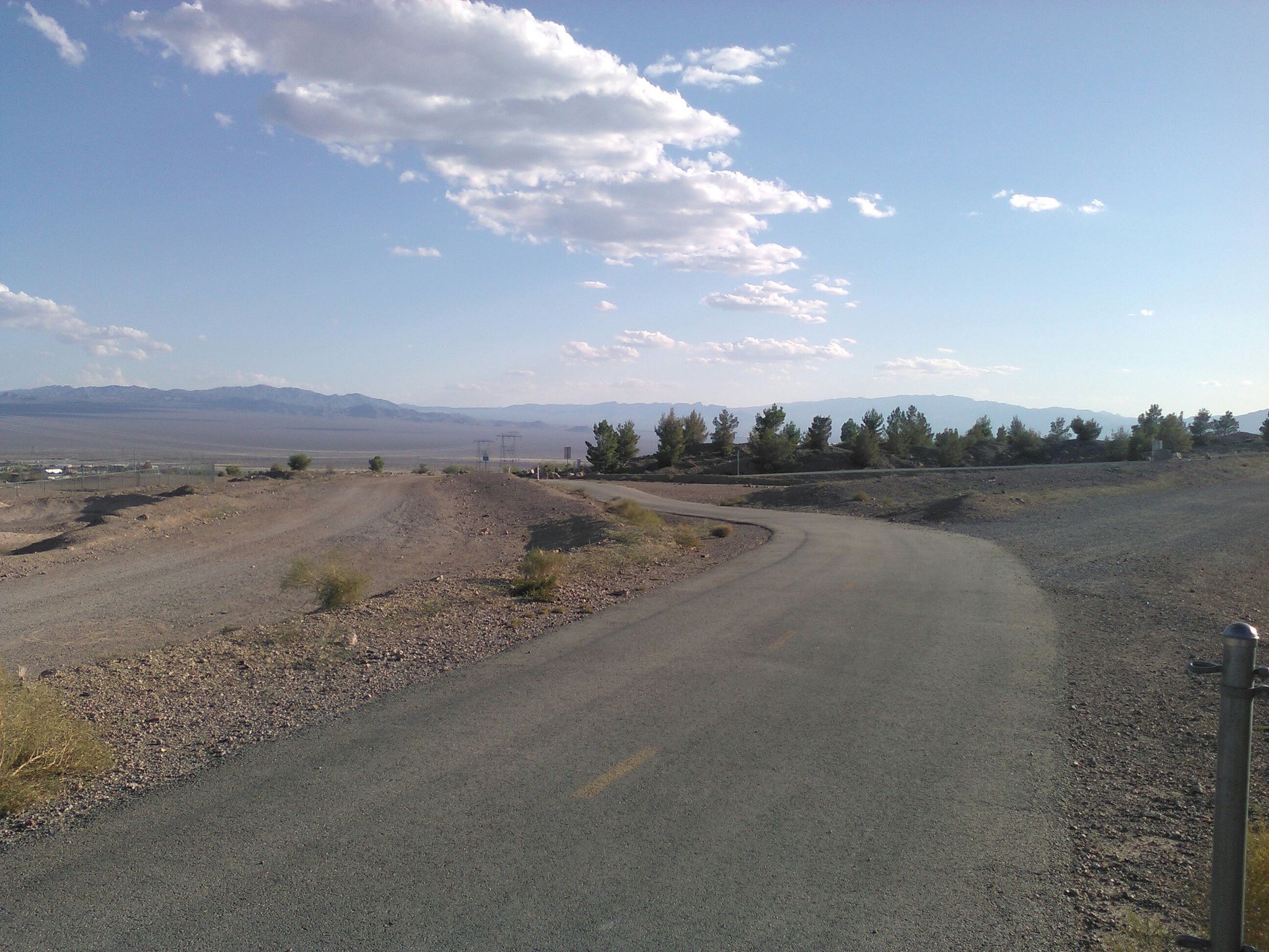 Paved road curves through arid desert landscape under a bright, cloudy sky. - River Mountains Loop Trail