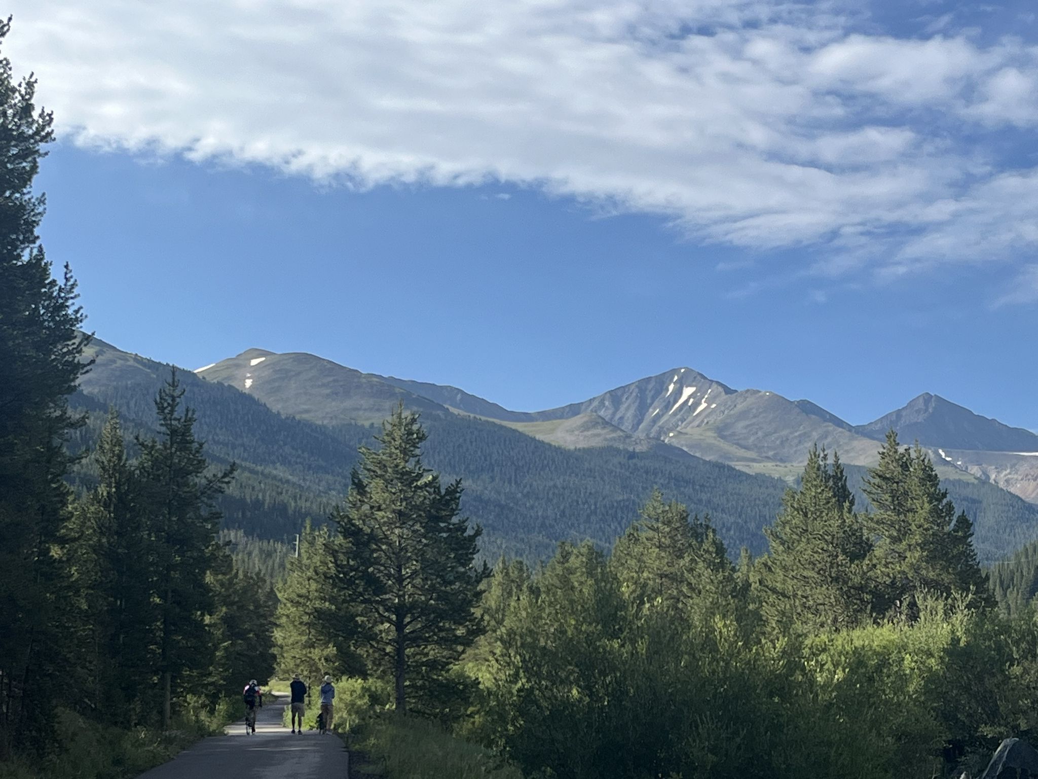 People walking on a paved road with forested mountains under a cloudy sky. - Fremont Pass Recreational Pathway