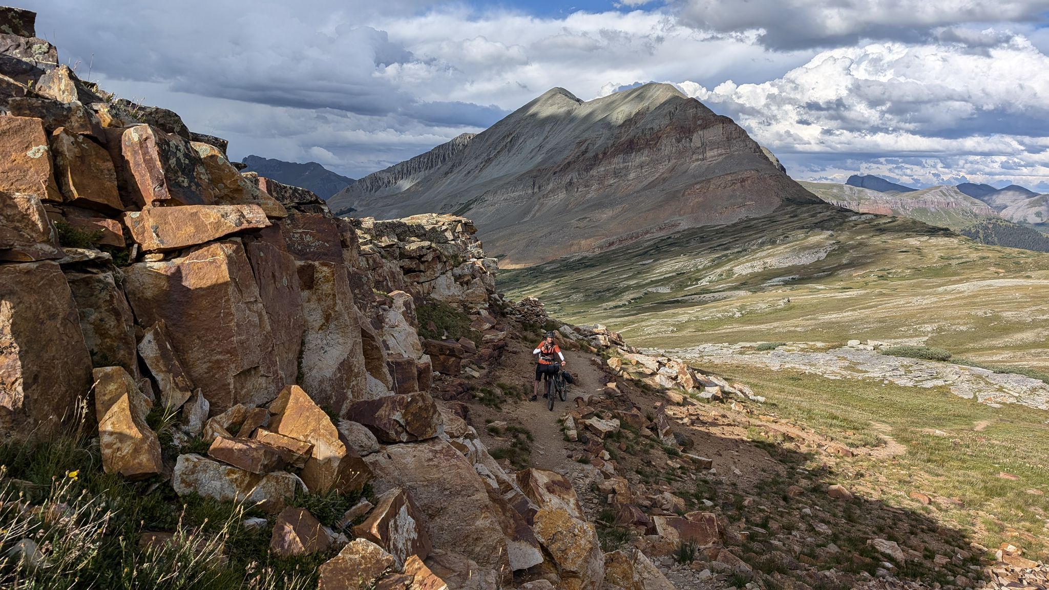 A mountain biker navigates a narrow, rocky trail on a steep mountain slope. - Lime Creek – Little Molas Lake loop from Little Molas Lake