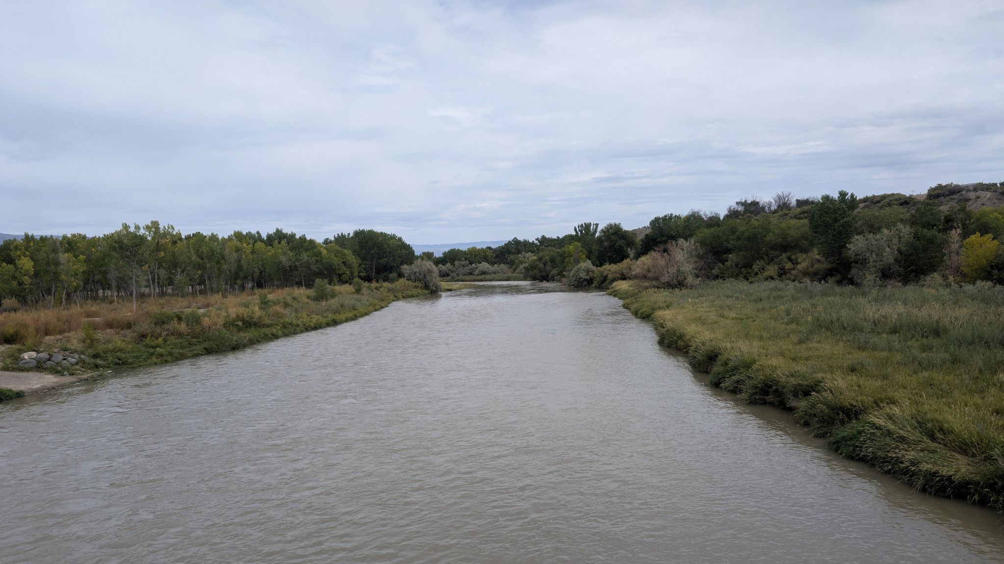 A wide river flows between lush green banks under an overcast sky. - Delta via Old Whitewater Road