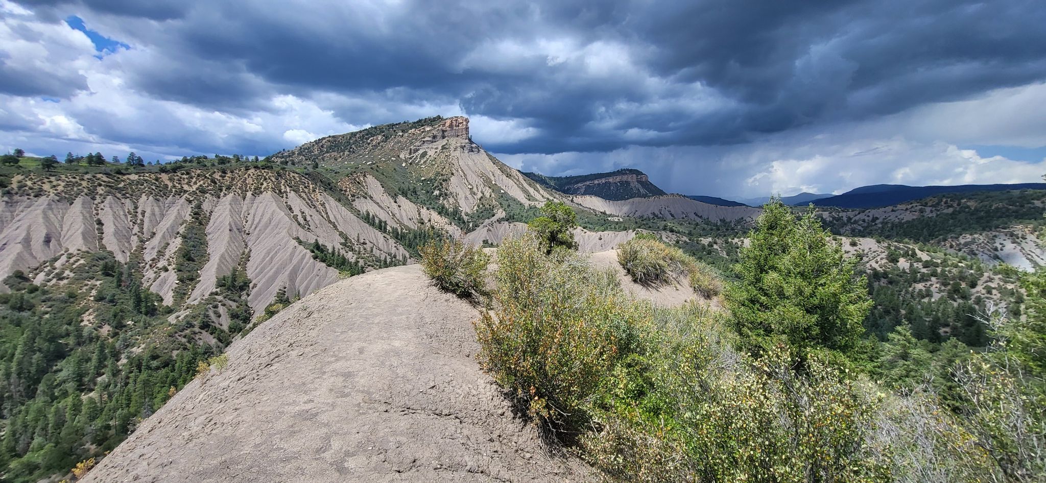 Dirt path on a ridge overlooking eroded mountains and a dramatic sky. - Hogsback Trail Loop