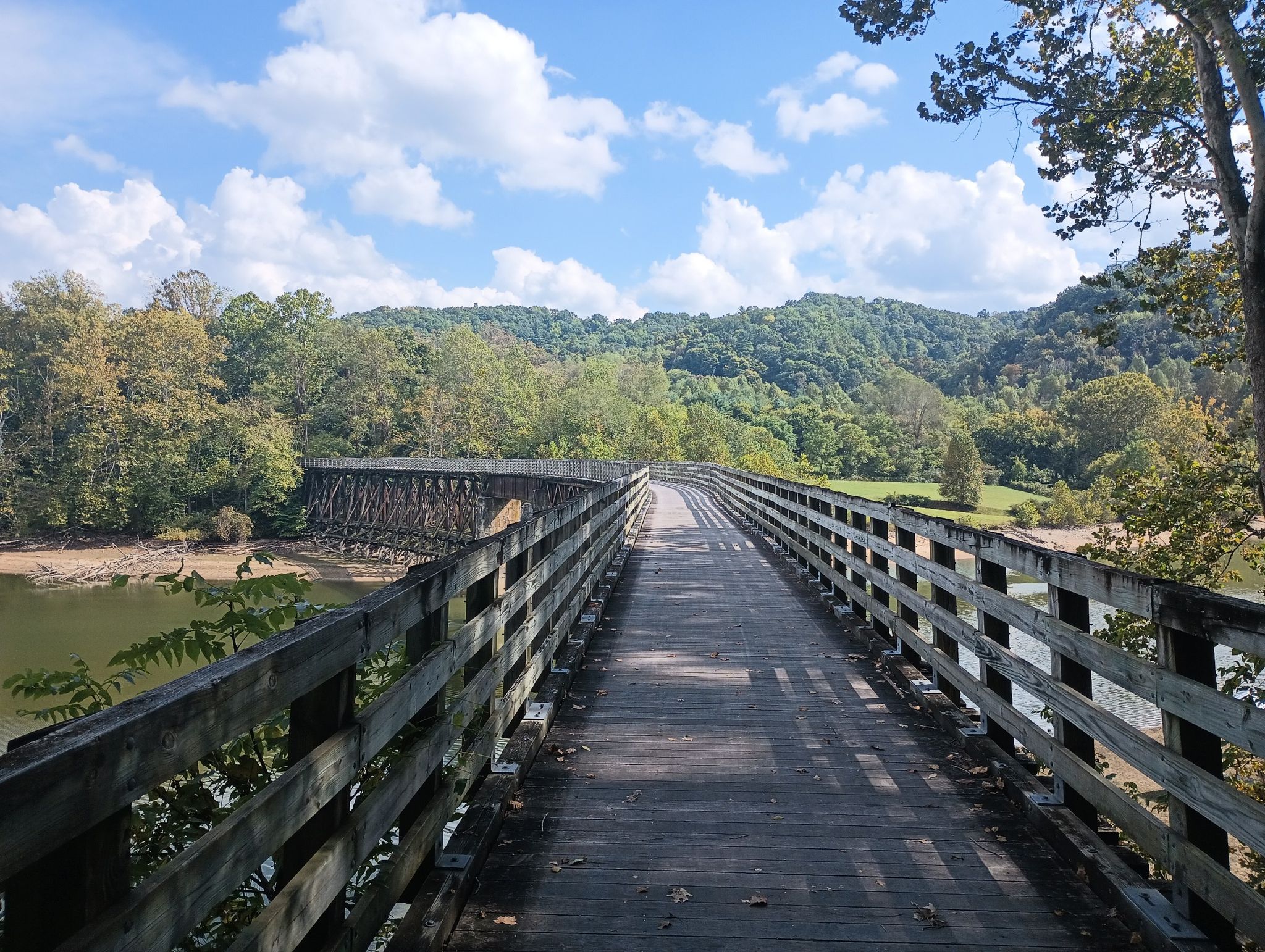 A long wooden bridge stretches over water, surrounded by green forested hills. - Damascus City Park – Holston River Confluence loop from Damascus