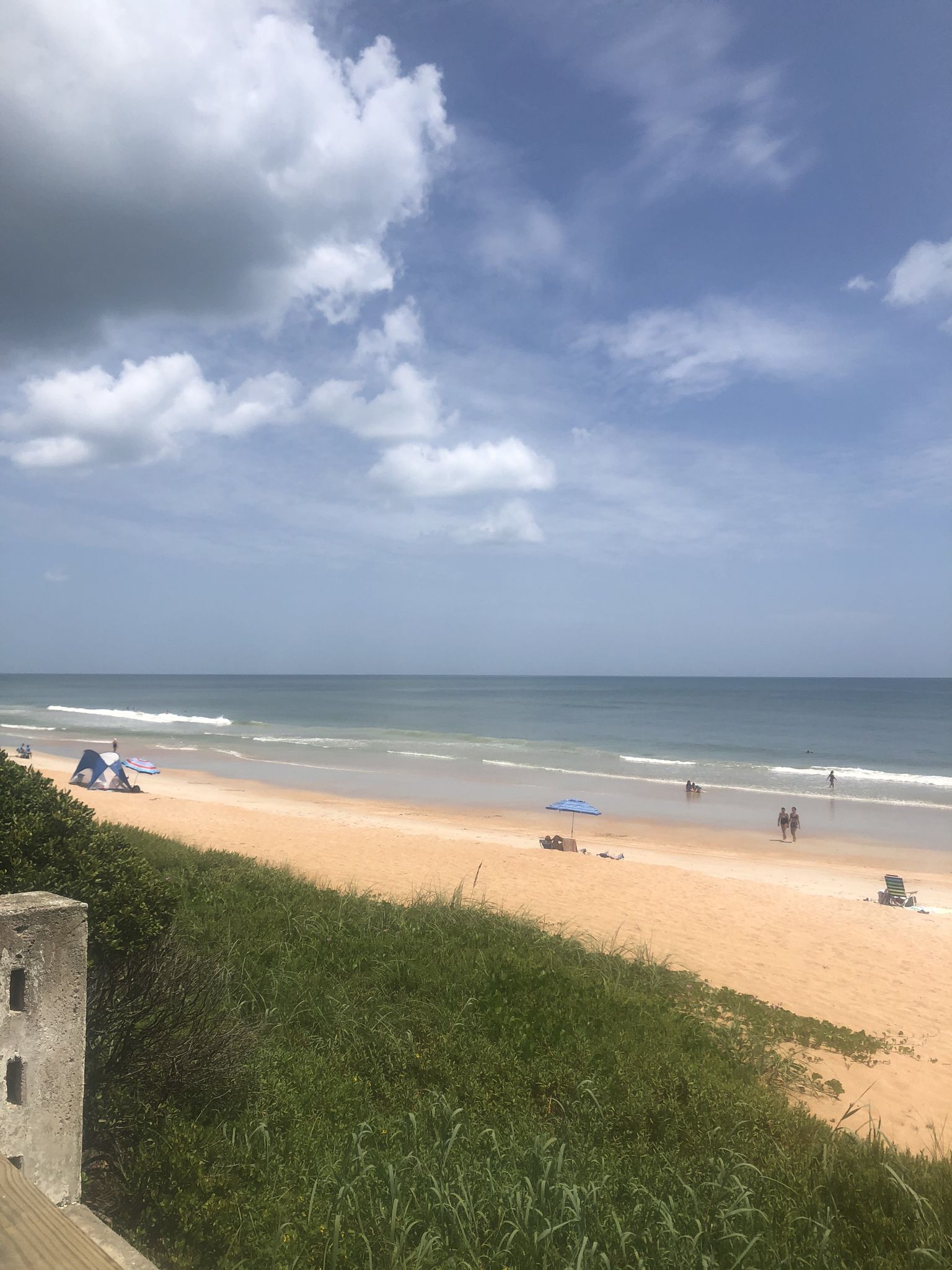 Sunny beach with people, ocean waves, and green dunes under a cloudy sky. - Ormond Beach to Flagler Beach Scenic Drive