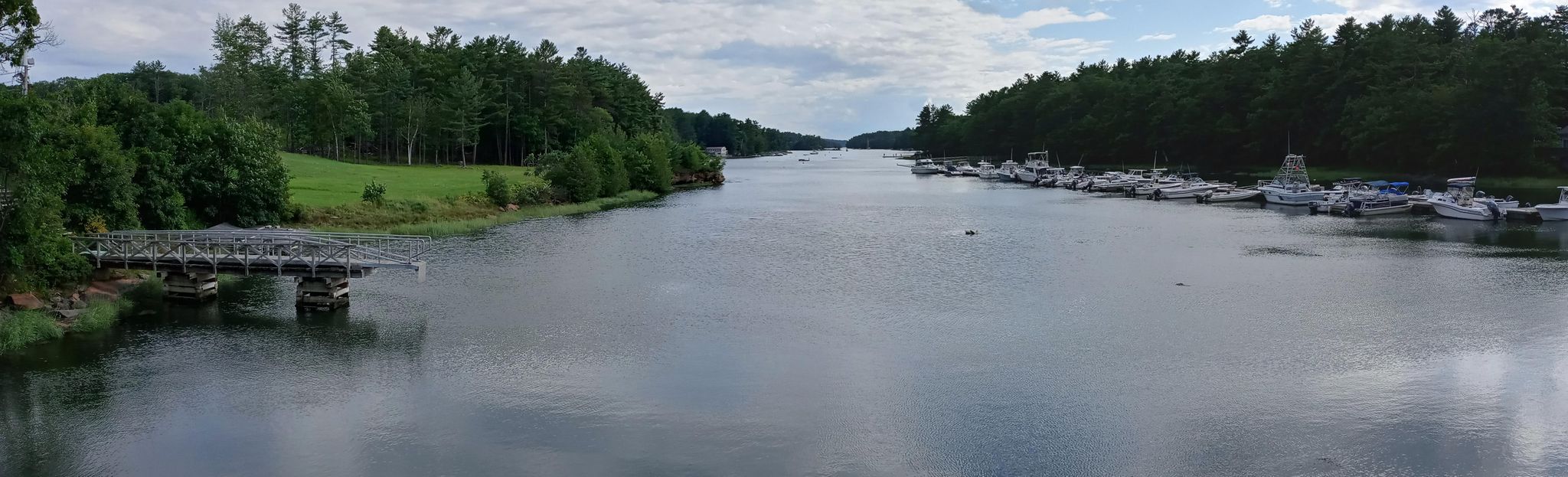 Wide river, boats docked, bridge, and forested banks under cloudy sky. - Androscoggin River Bike Path – Spectacular mud flats loop from Lisbon