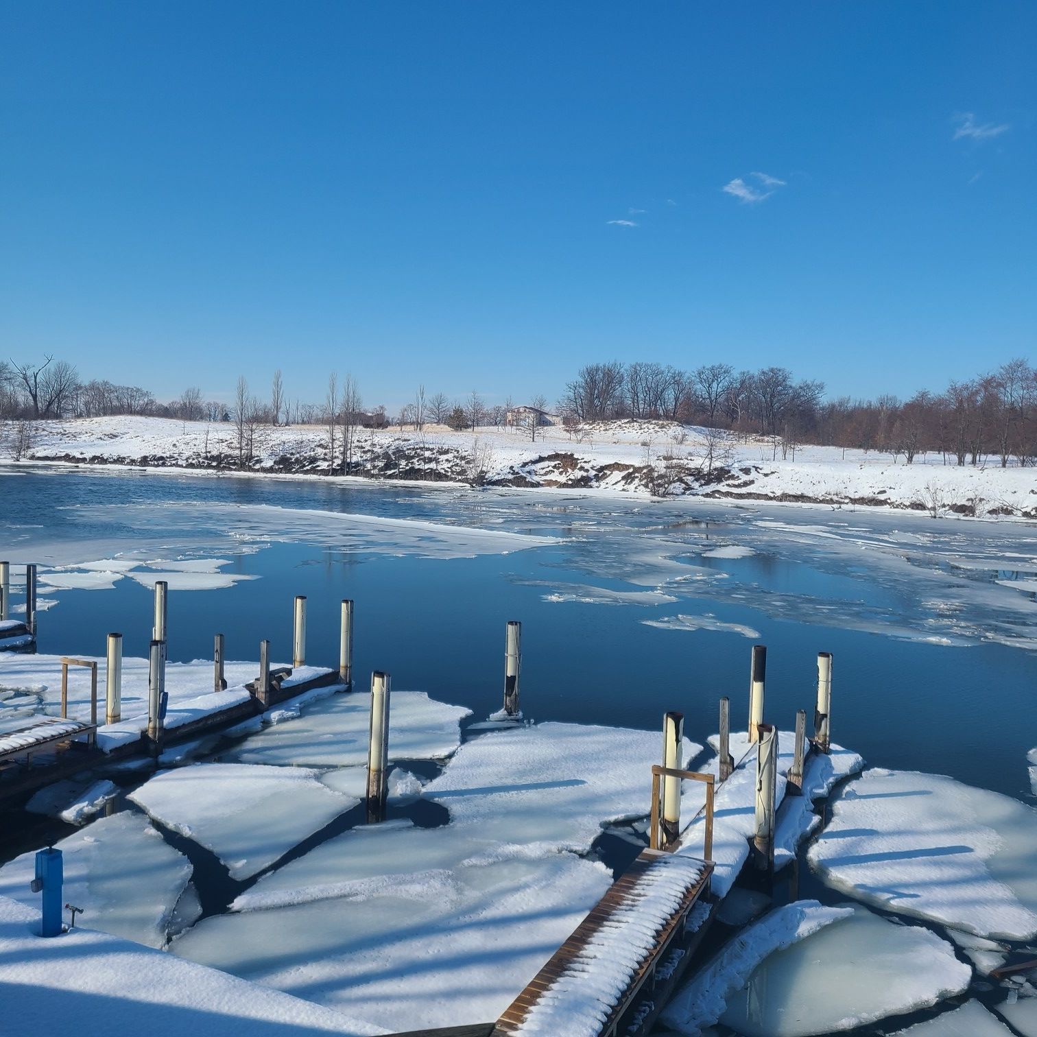 Icy river with wooden docks and snowy banks under a bright blue sky. - Manistee River Walk