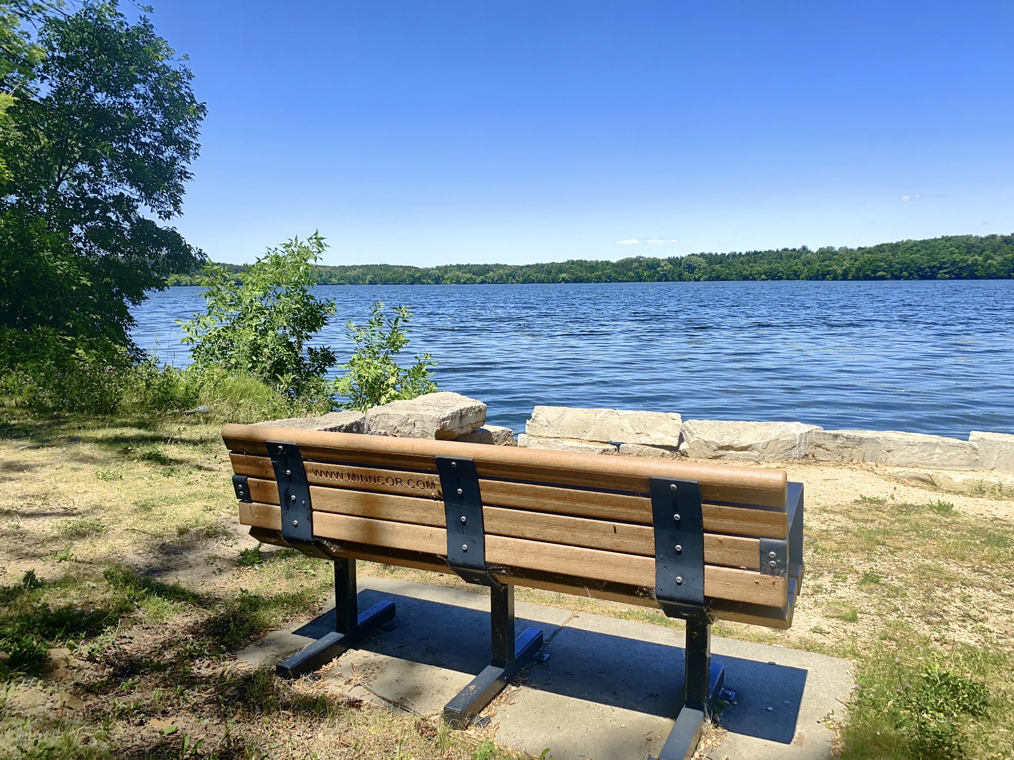 Empty wooden park bench facing a wide lake under a clear blue sky. - Vadnais-Snail Lakes Regional Park run