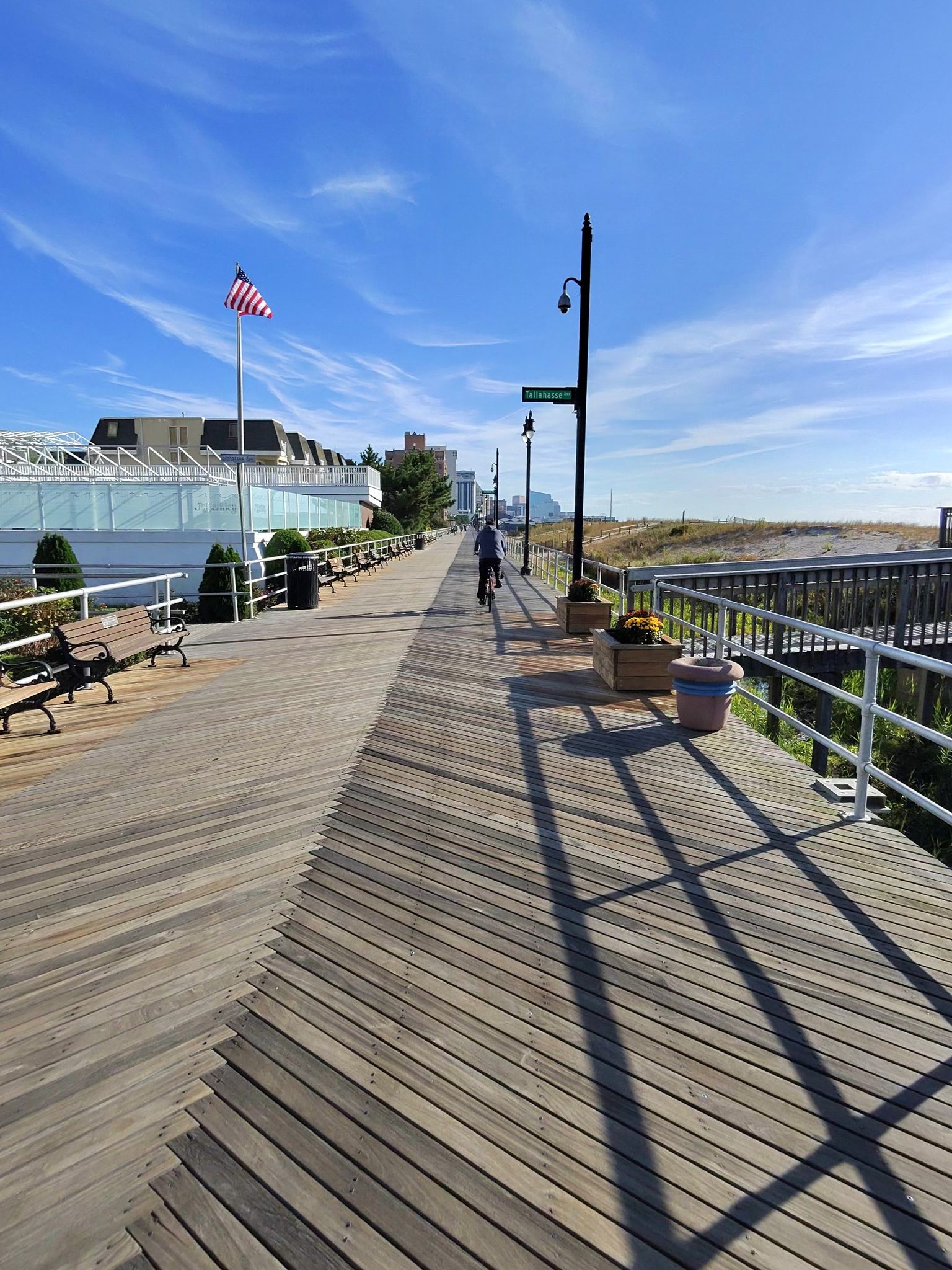 Sunny wooden boardwalk with a person cycling, American flag, and distant ocean. - Pleasantville to Ocean City