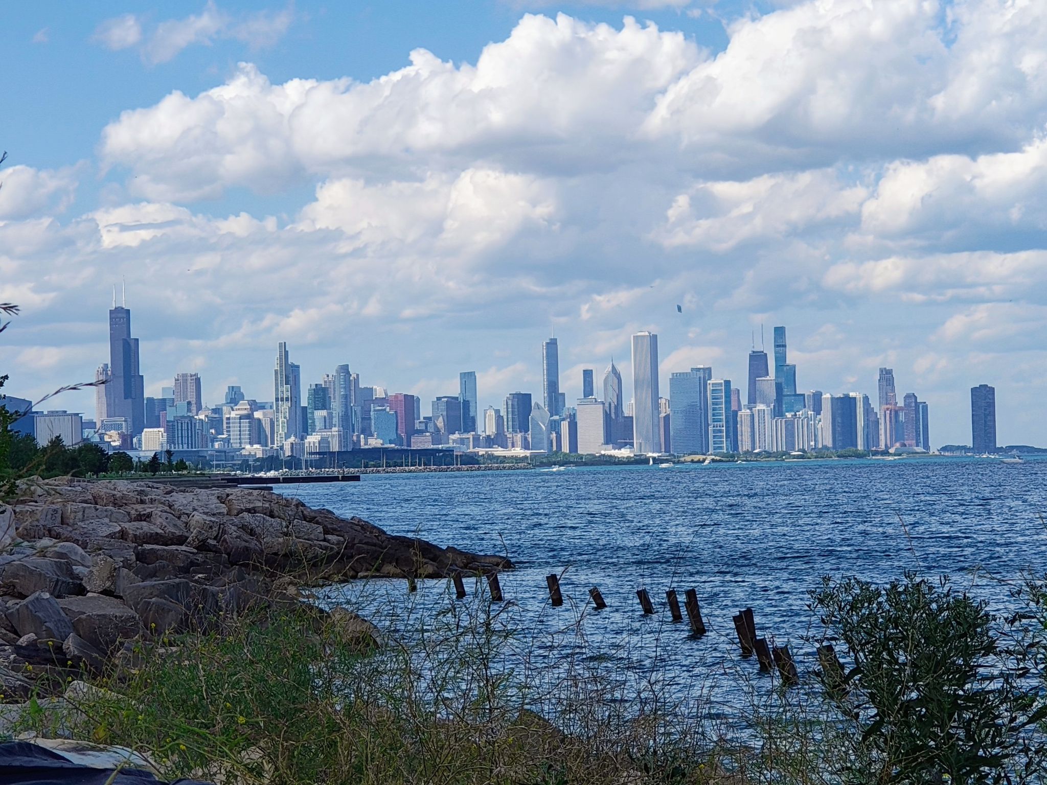 Rocky shore and blue water with a distant city skyline under a cloudy sky. - Lakefront Trail