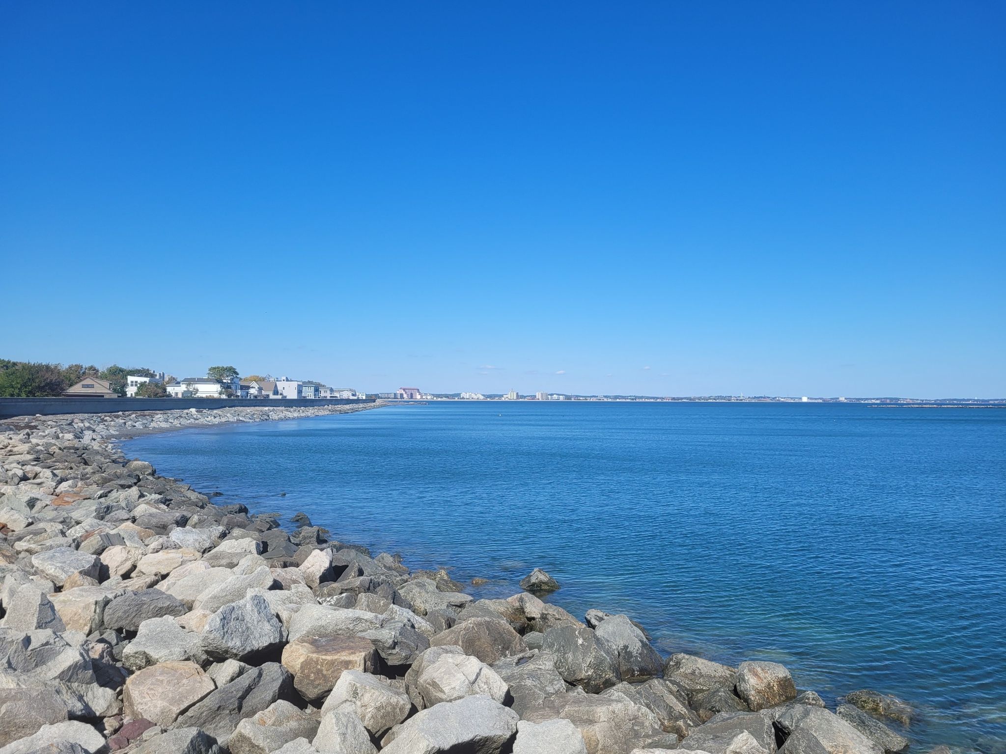Rocky shoreline next to a calm blue ocean under a clear sky. - Revere Beach