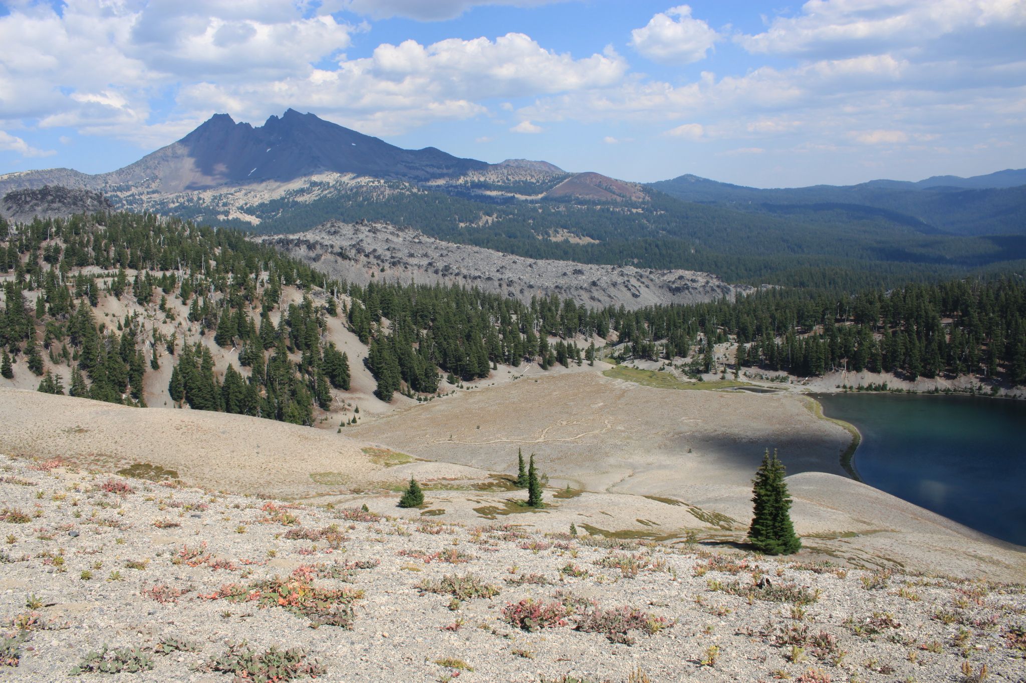 A clear blue lake nestled among forested hills with a large mountain in background. - South Sister Climber Trail