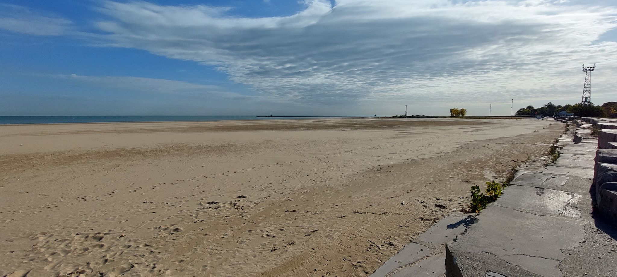 Expansive sandy beach next to calm water under a partly cloudy sky. - Montrose Beach Dunes Natural Area loop