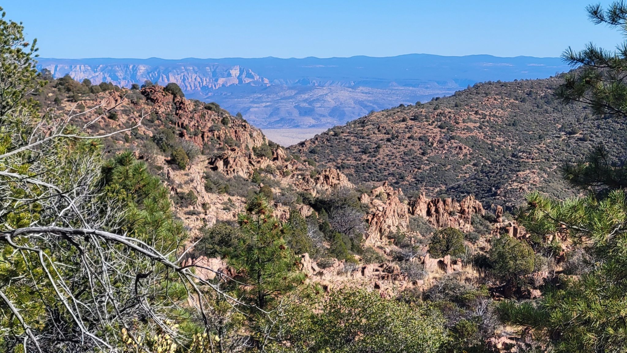 Rocky canyon with distant mountains and a valley under a bright blue sky. - North Mingus Trail #105