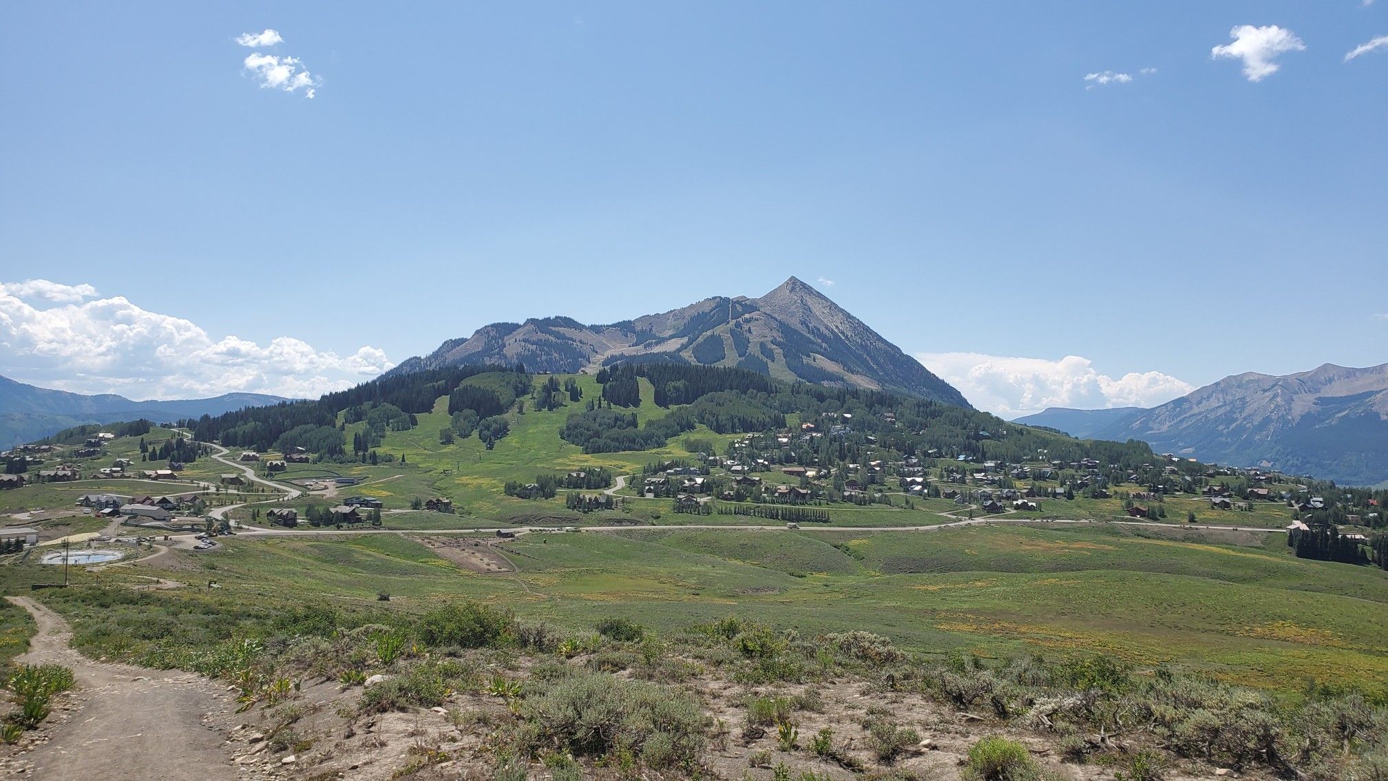 A town sits at the base of a large mountain under a clear blue sky. - Teddy's Trail