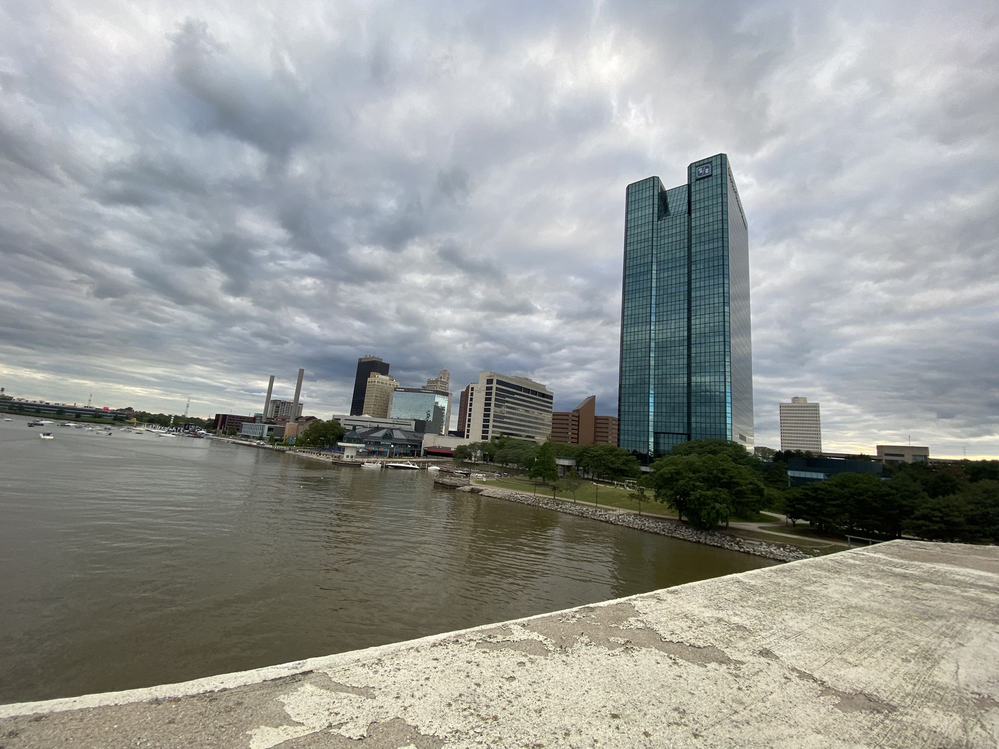 City skyline with a tall glass building next to a river under cloudy skies. - Main Street Bridge loop from Toledo