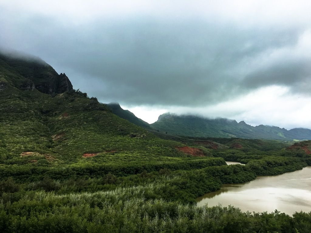 Lush green mountains and a river under a dramatic, cloudy sky. - View of Haʻupu Ridge loop from Lihue