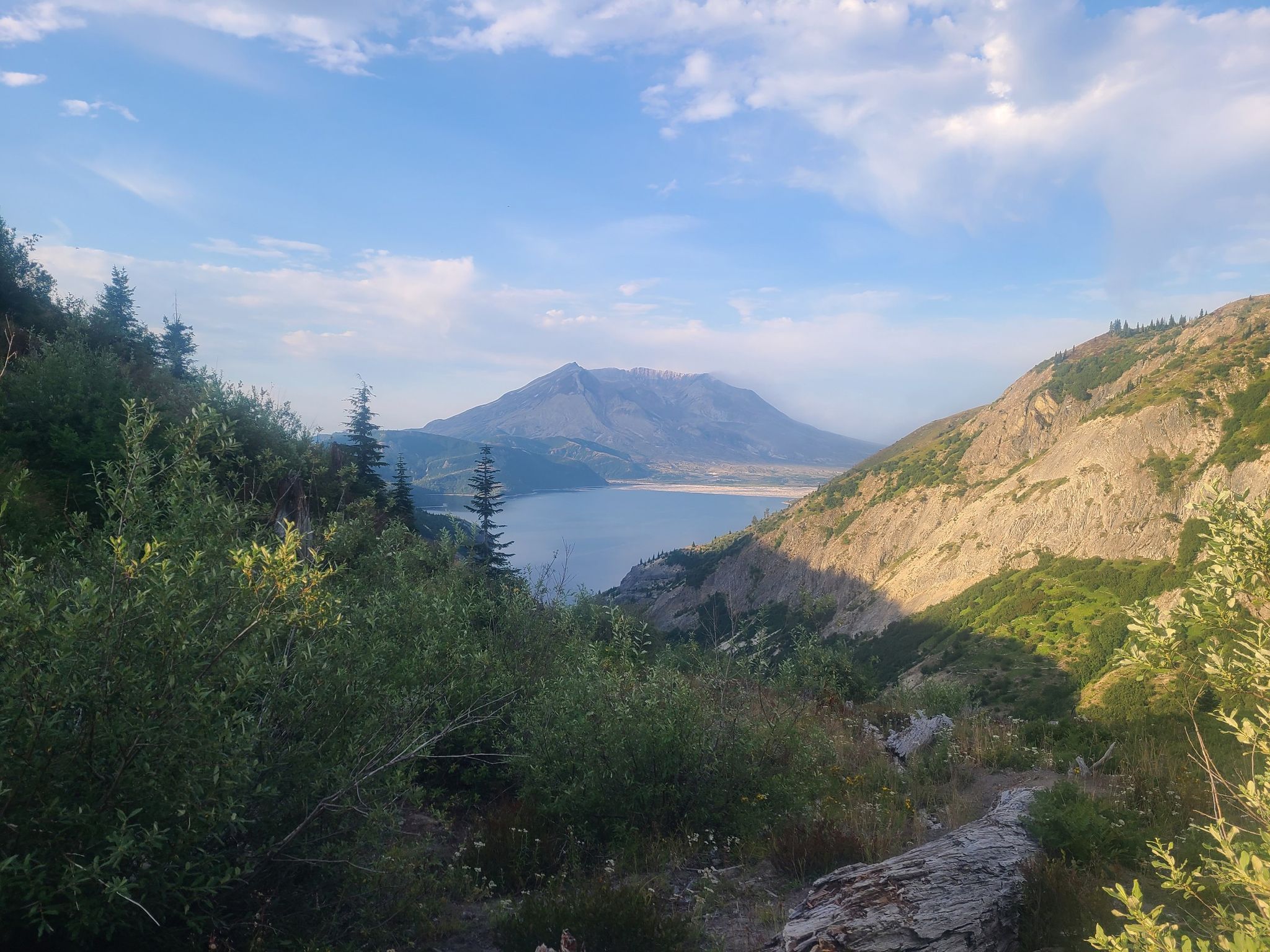 Distant mountain and lake framed by green valley slopes under clouds. - Norway Pass via Boundary Trail