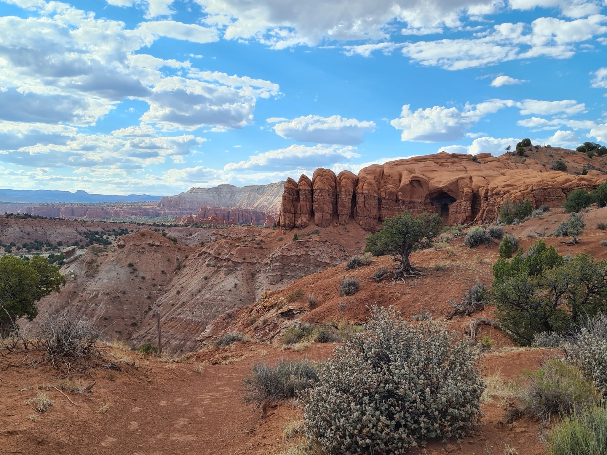 Expansive desert landscape with red rock formations under a bright, cloudy sky. - Shakespeare Arch – Sentinel Trail