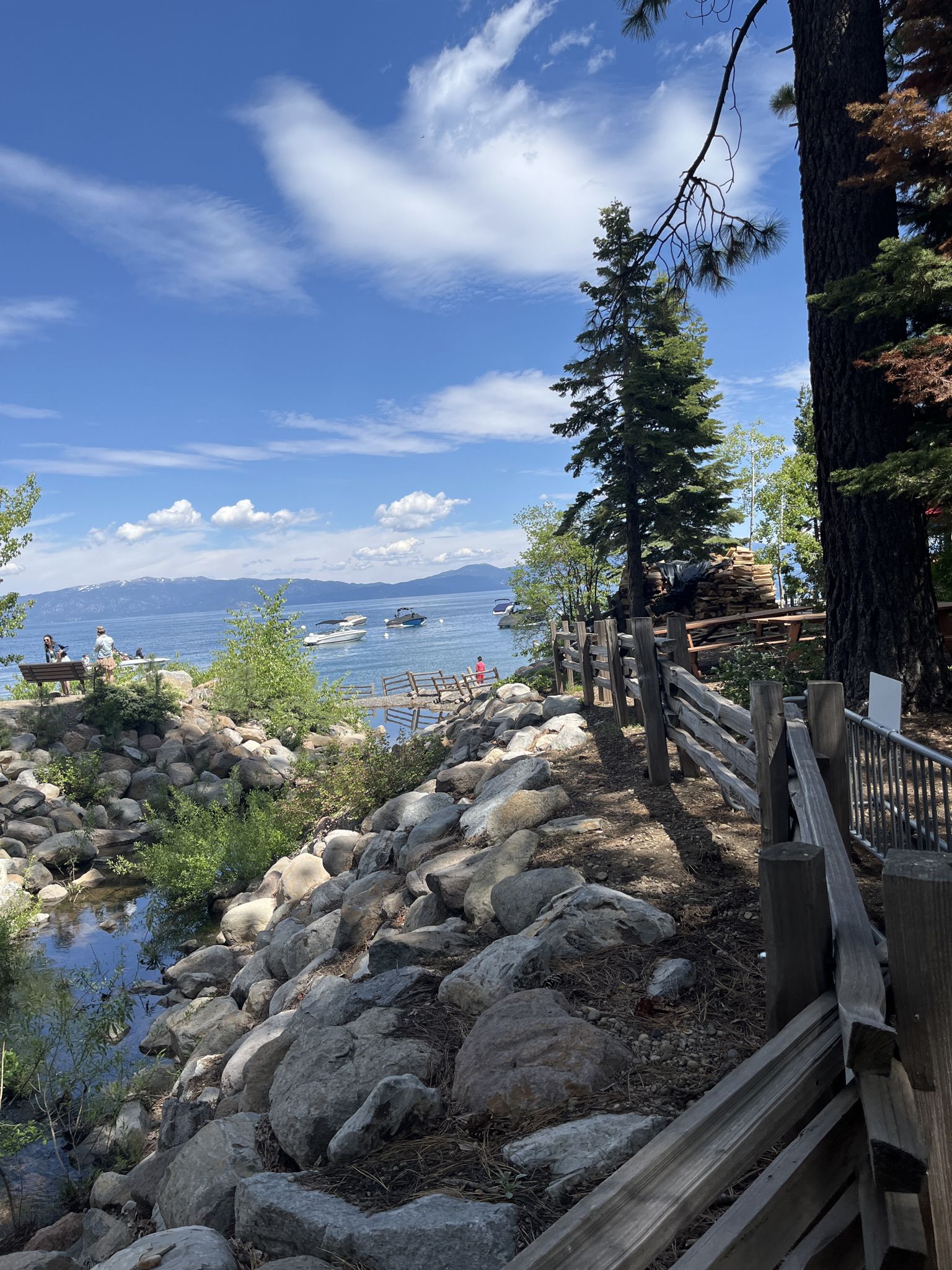 Sunny view of a rocky path, lake with boats, and distant mountains. - West Shore Bike Path