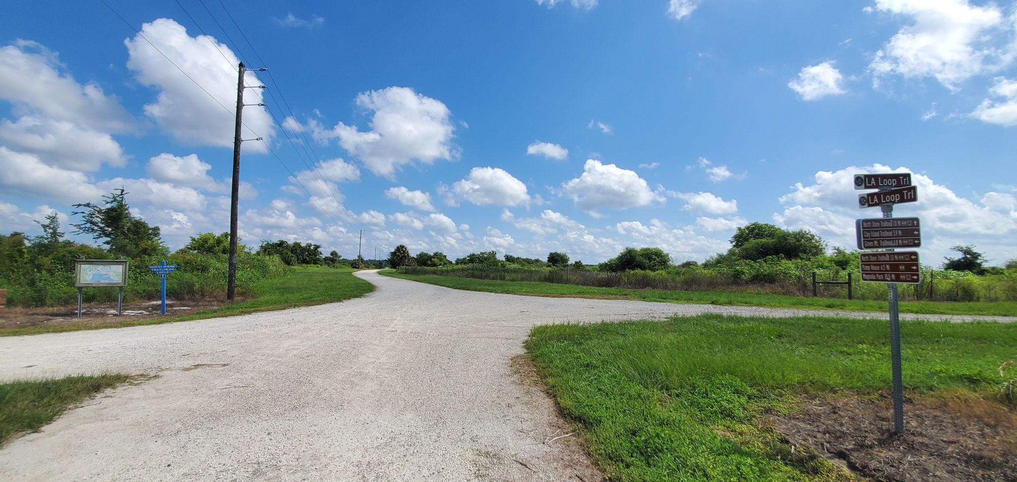 A fork in a dirt road with signposts and power pole under blue sky. - Lake Apopka Loop Trail
