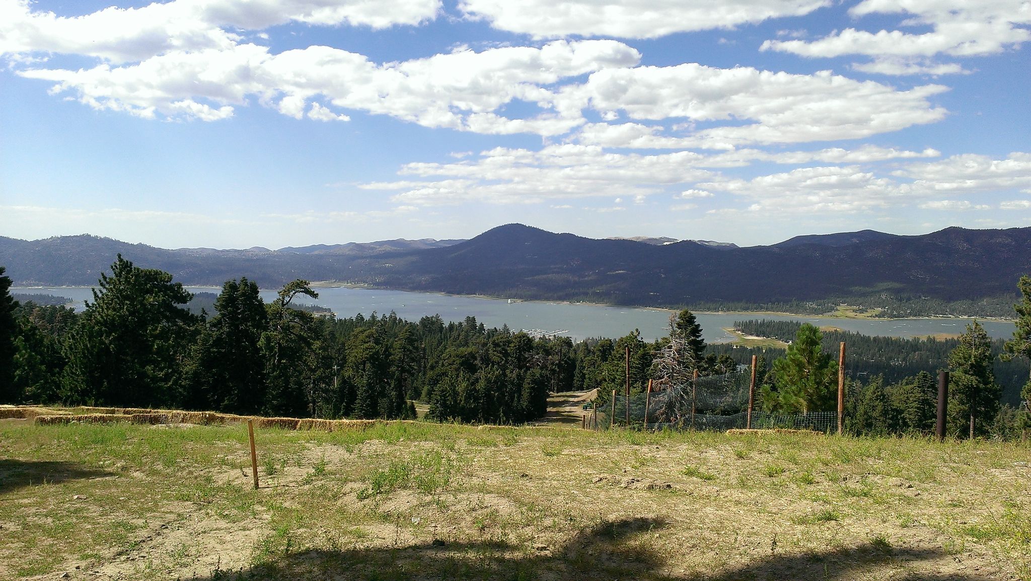 Panoramic view of a large lake surrounded by mountains and forests under a cloudy sky. - Snow Summit Skyline and Going Green Loop