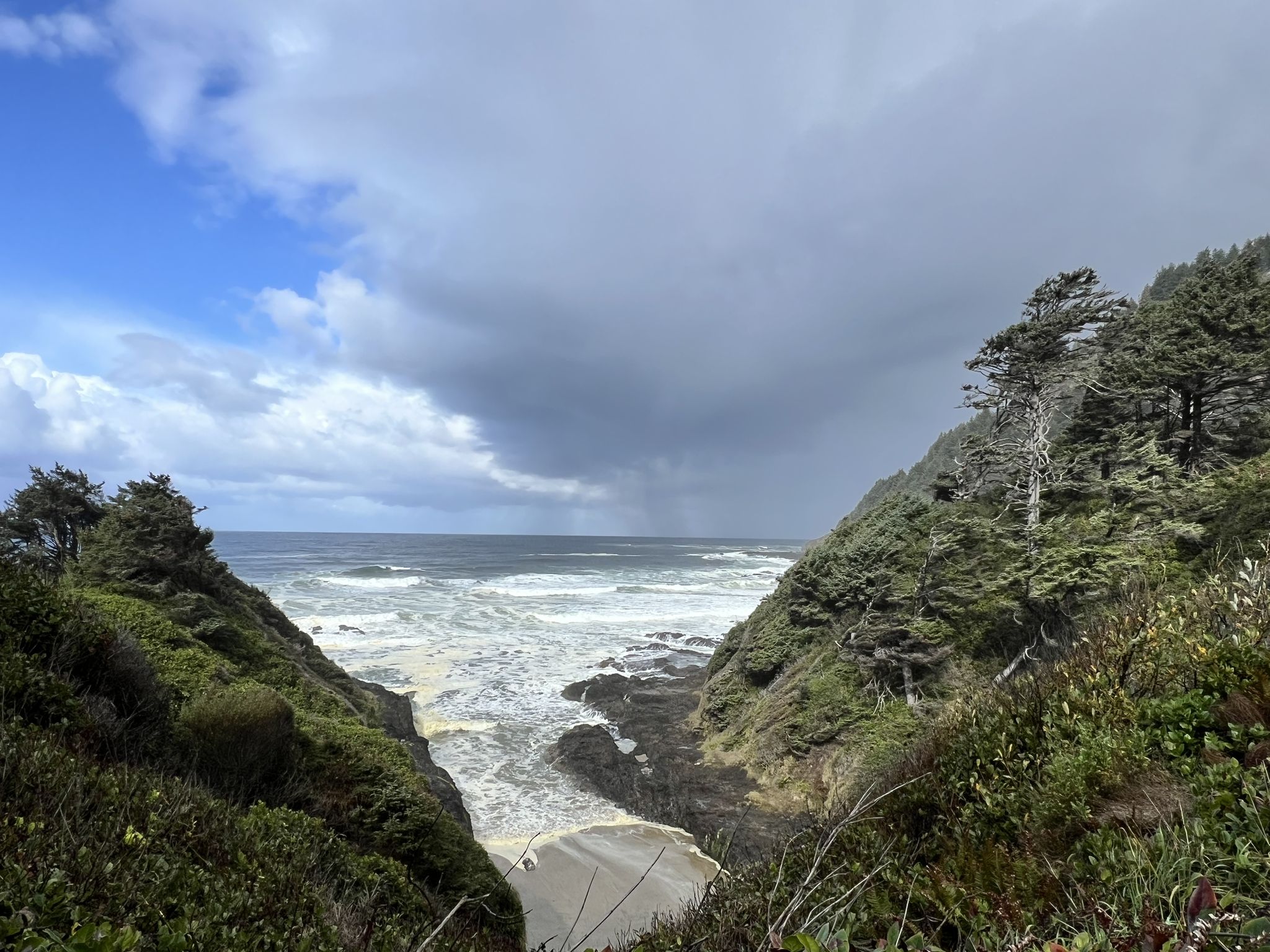 A stormy sky hangs over a rocky ocean cove with crashing waves. - Cape Perpetua Visitor Center – Cape Cove Beach loop from Cape Perpetua Special Interest Area