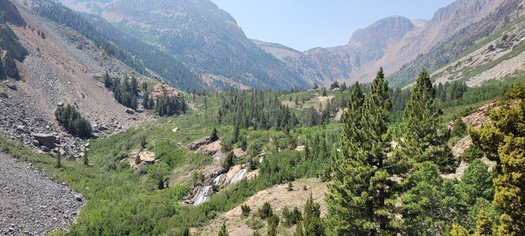Expansive mountain valley with dense green forest, distant peaks, and a small waterfall. - Lundy Canyon Trail