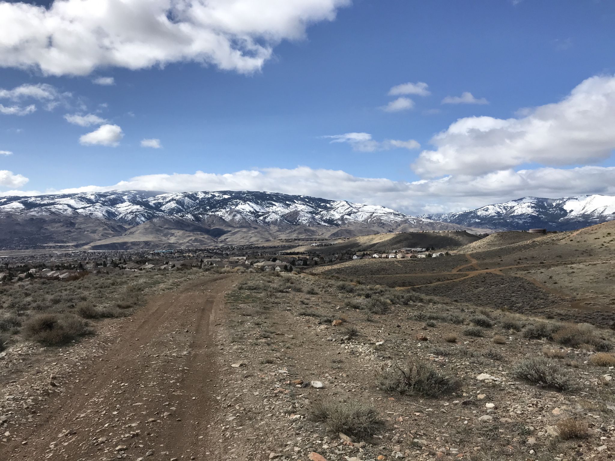 Dirt road through arid hills towards snow-capped mountains under a partly cloudy sky. - Peavine Trail Network Loop