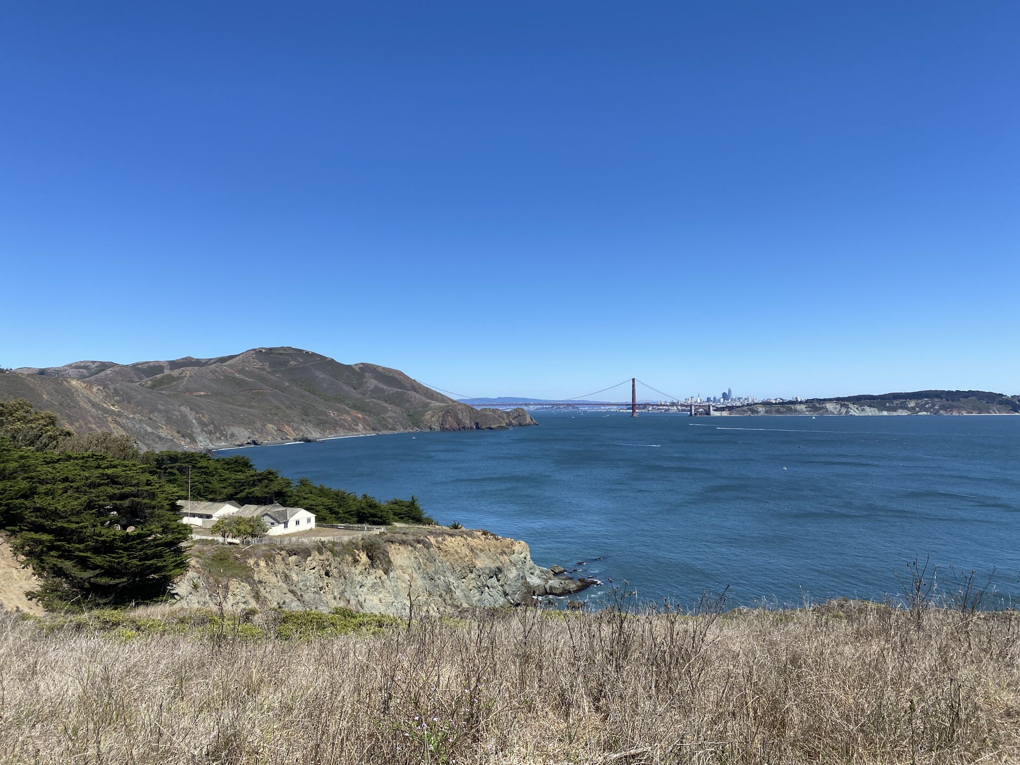 Sunny bay with distant bridge, mountains, and coastal homes. - Point Bonita Trail Loop