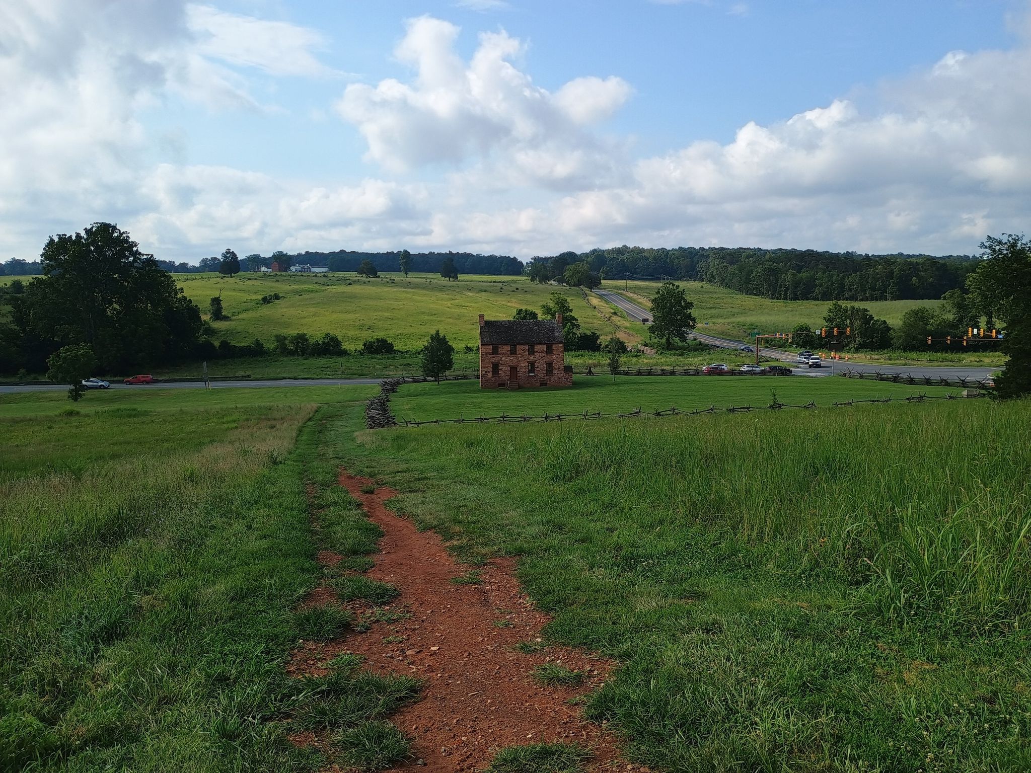 Dirt path leading to a stone house in a green field under a cloudy sky. - Second Manassas Trail