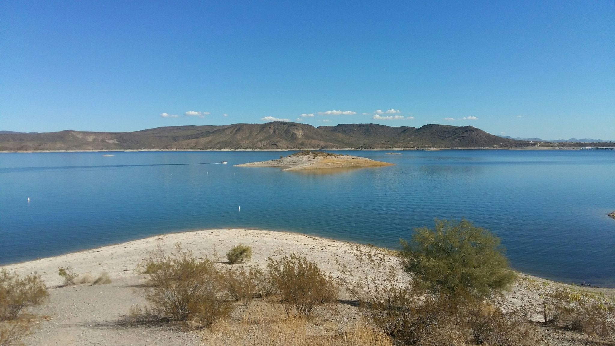 Expansive blue lake with a small island and distant mountains under clear sky. - Wild Burro Trail Loop